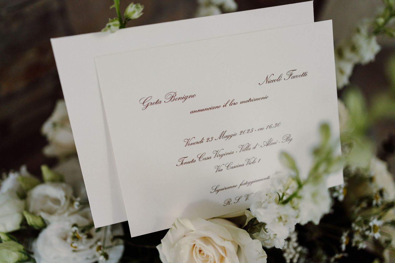 Wedding invitation cards surrounded by white roses and delicate floral arrangements.