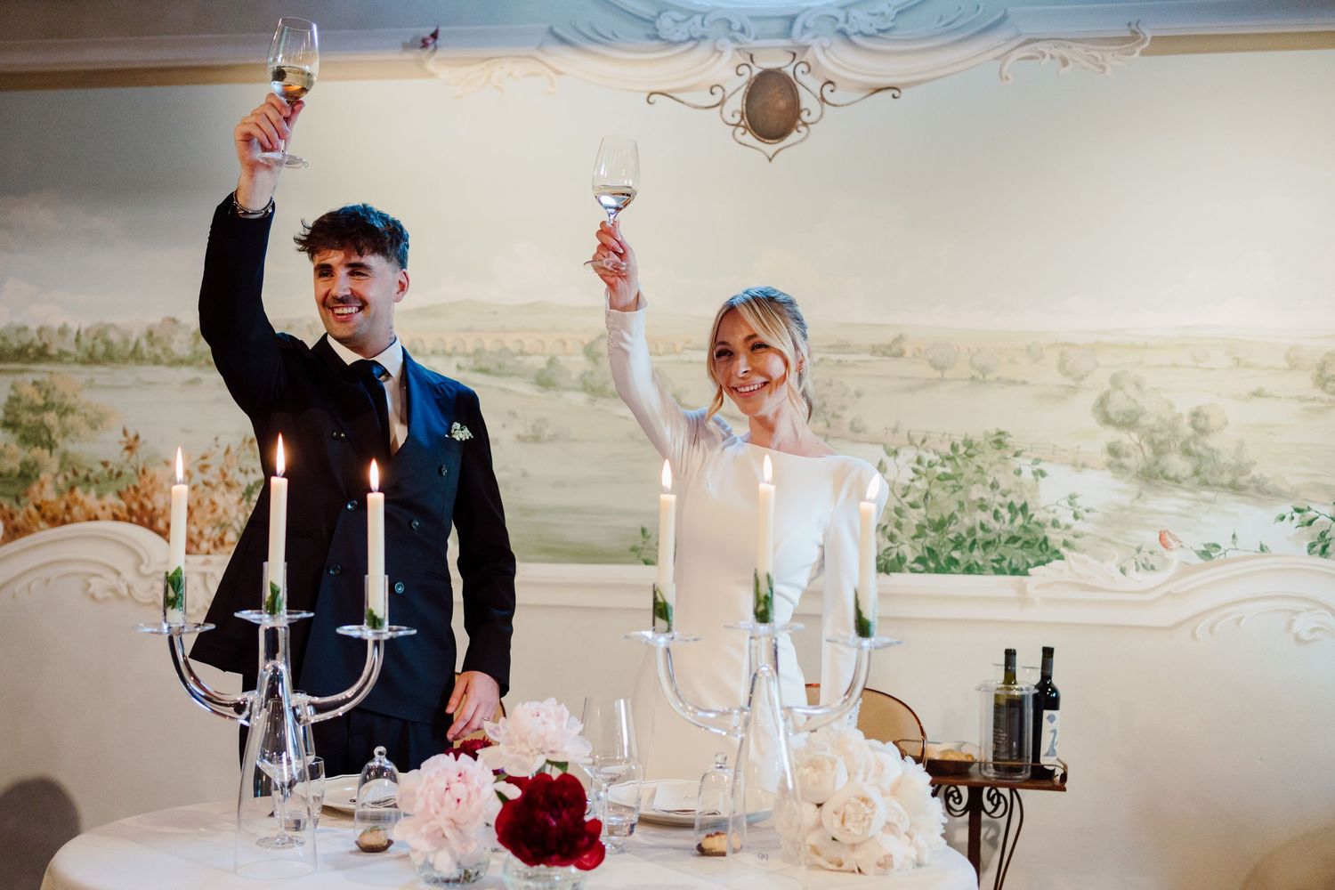 Bride and groom raising champagne glasses in a toast at their sweetheart table with candles.