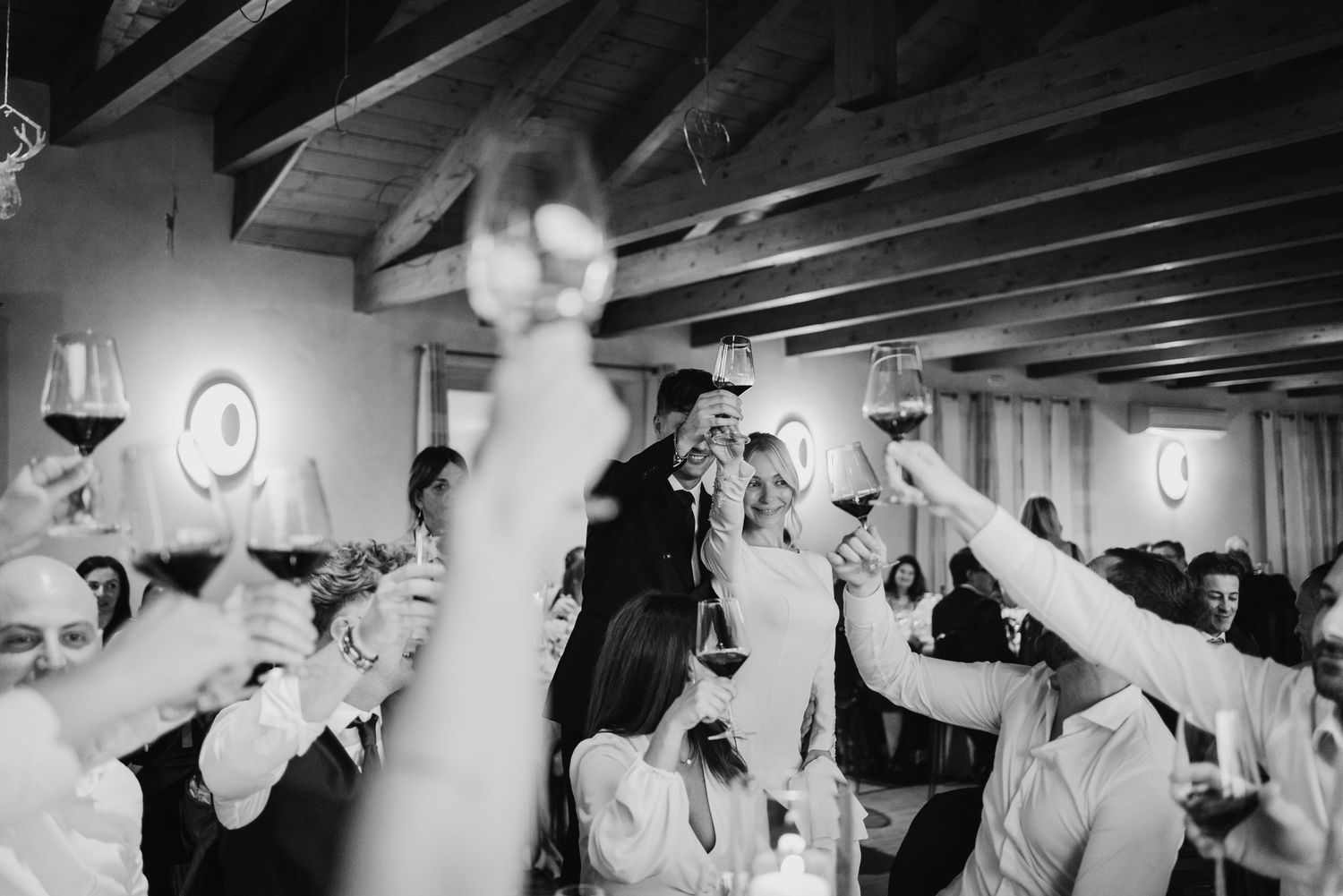 Wedding guests enthusiastically raising glasses of red wine in a celebratory toast.