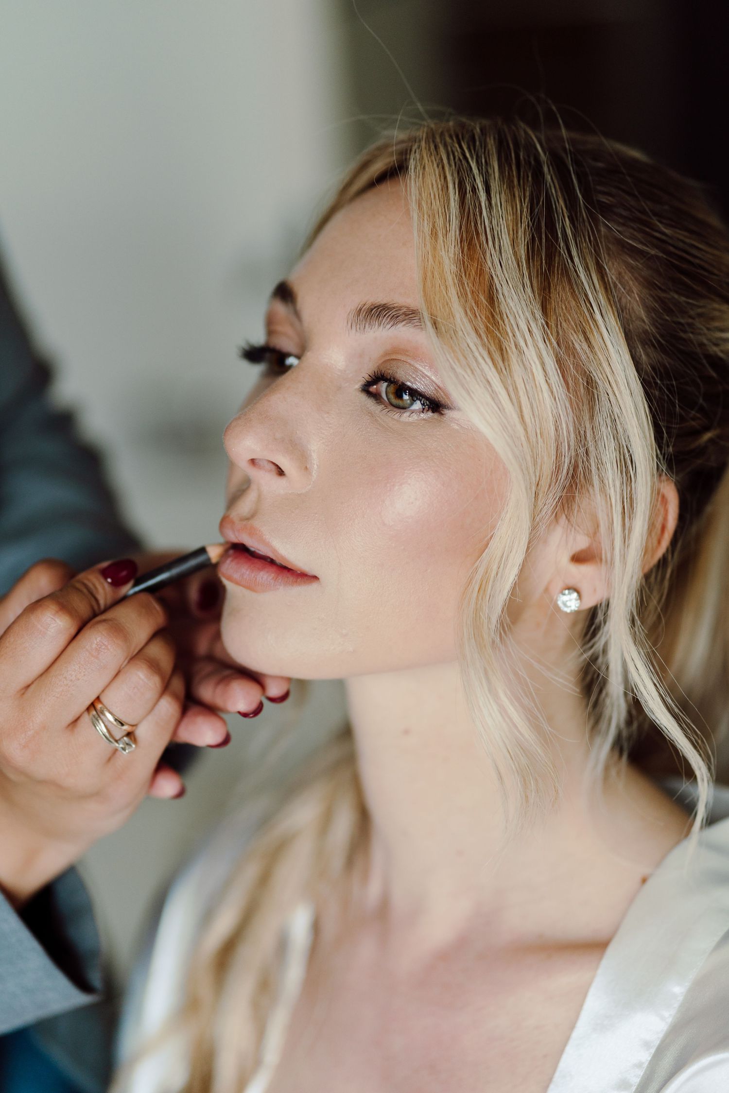 Makeup artist applying lip liner to a blonde bride during wedding preparations.