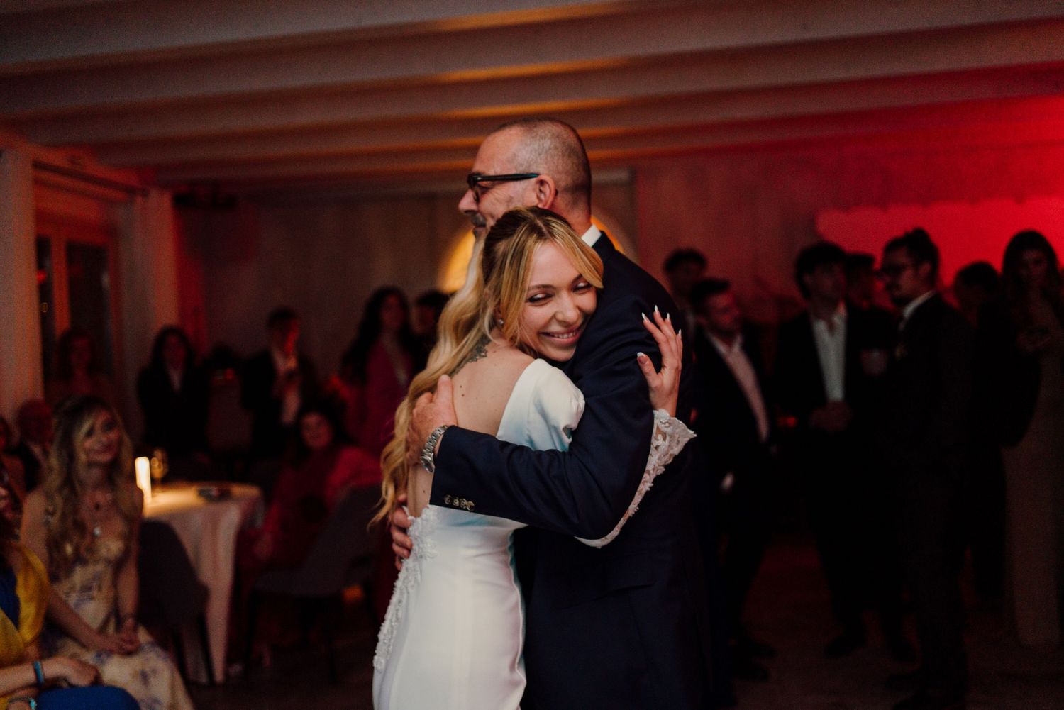 Bride sharing a warm emotional hug with older man on the dance floor during wedding reception.