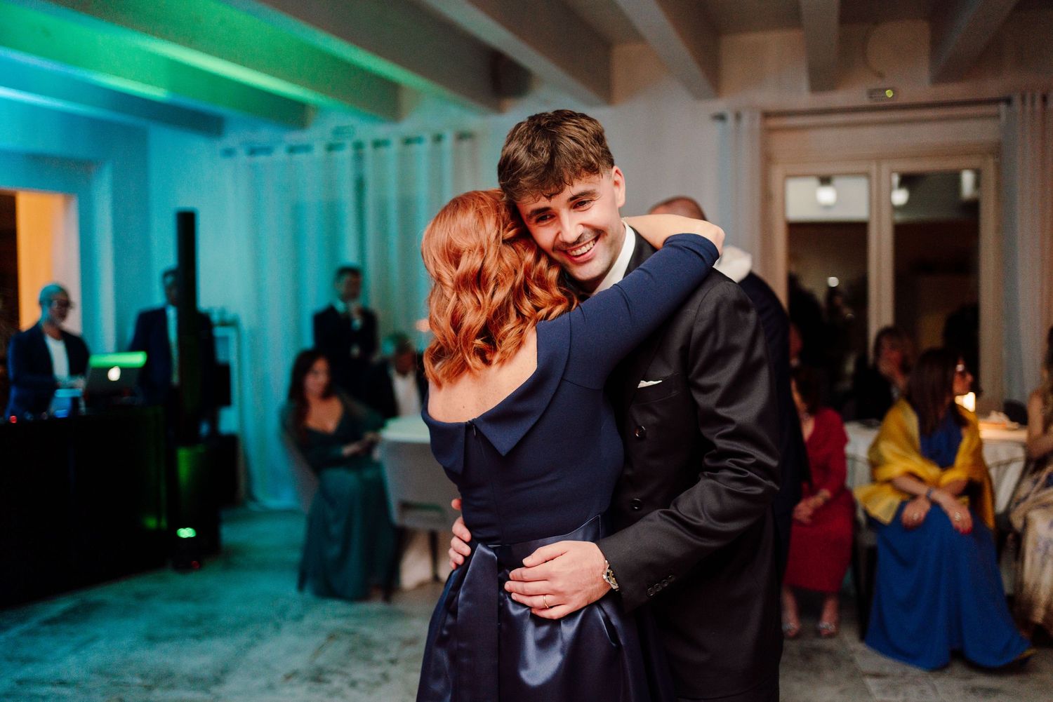 Couple sharing a joyful dance embrace under teal lighting at an elegant indoor wedding reception.