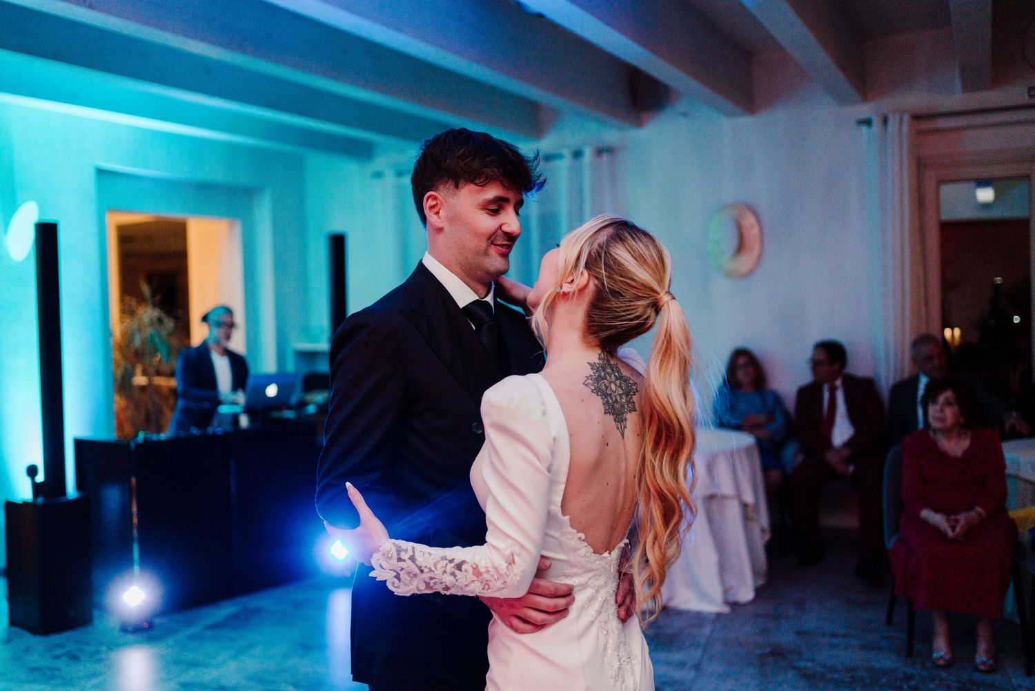 Bride and groom sharing their first dance under blue lighting with guests watching at wedding reception.