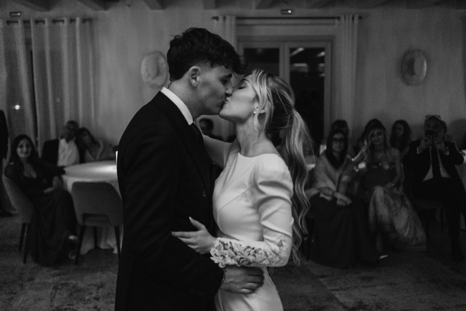 Black and white photo of bride and groom sharing a kiss during first dance at wedding reception.