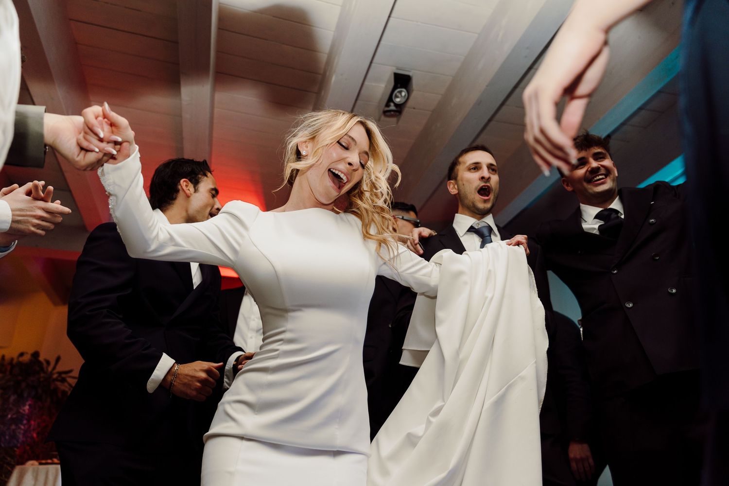 Joyful bride in elegant white gown dances energetically with wedding guests at reception.