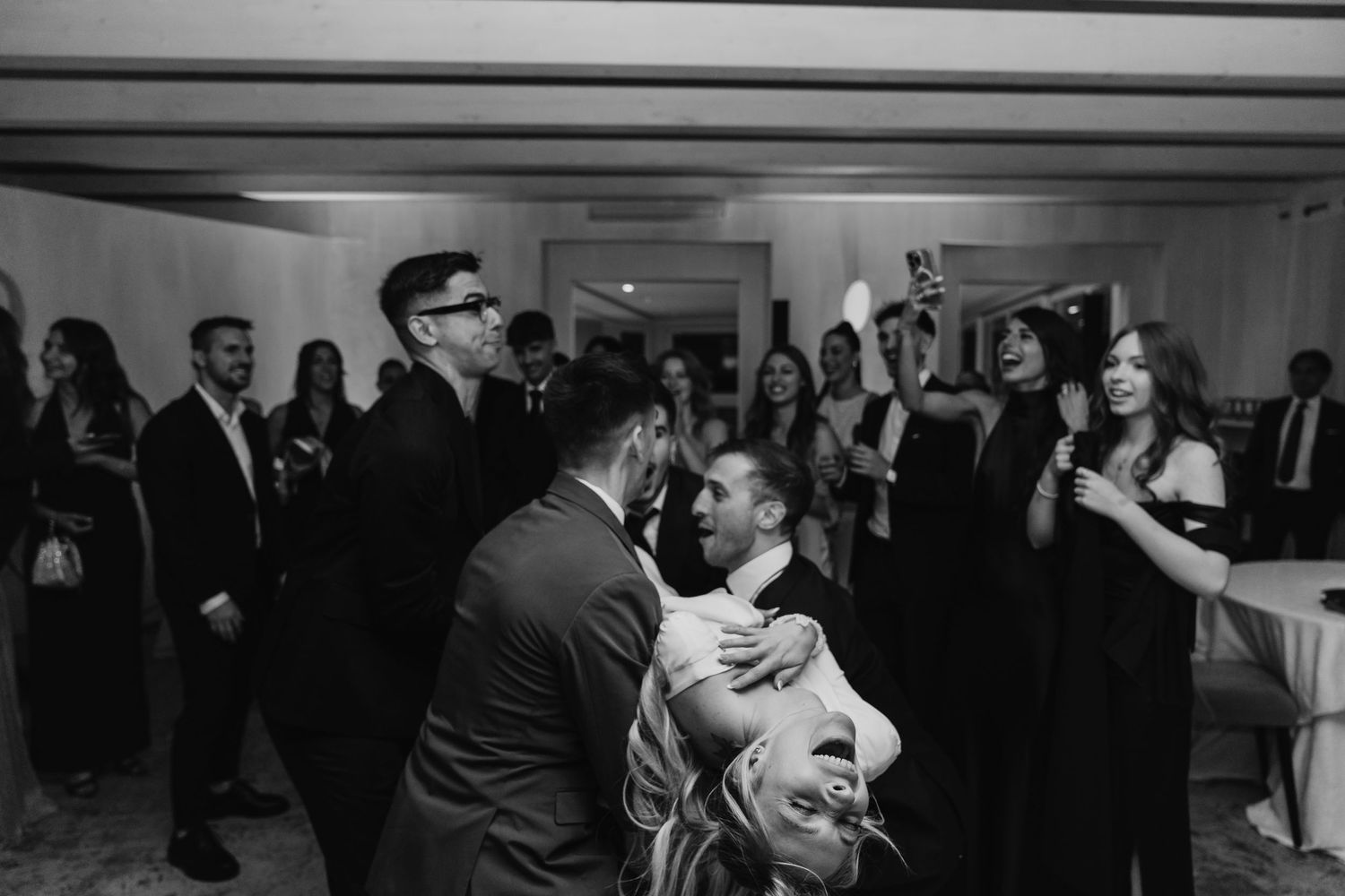 Black and white photo of groomsmen lifting bride during lively wedding reception dancing.