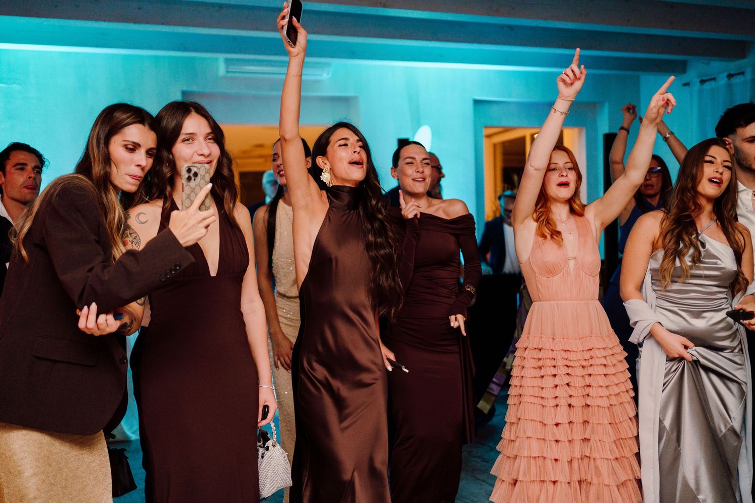 Group of elegantly dressed women celebrating and dancing together at a wedding reception.