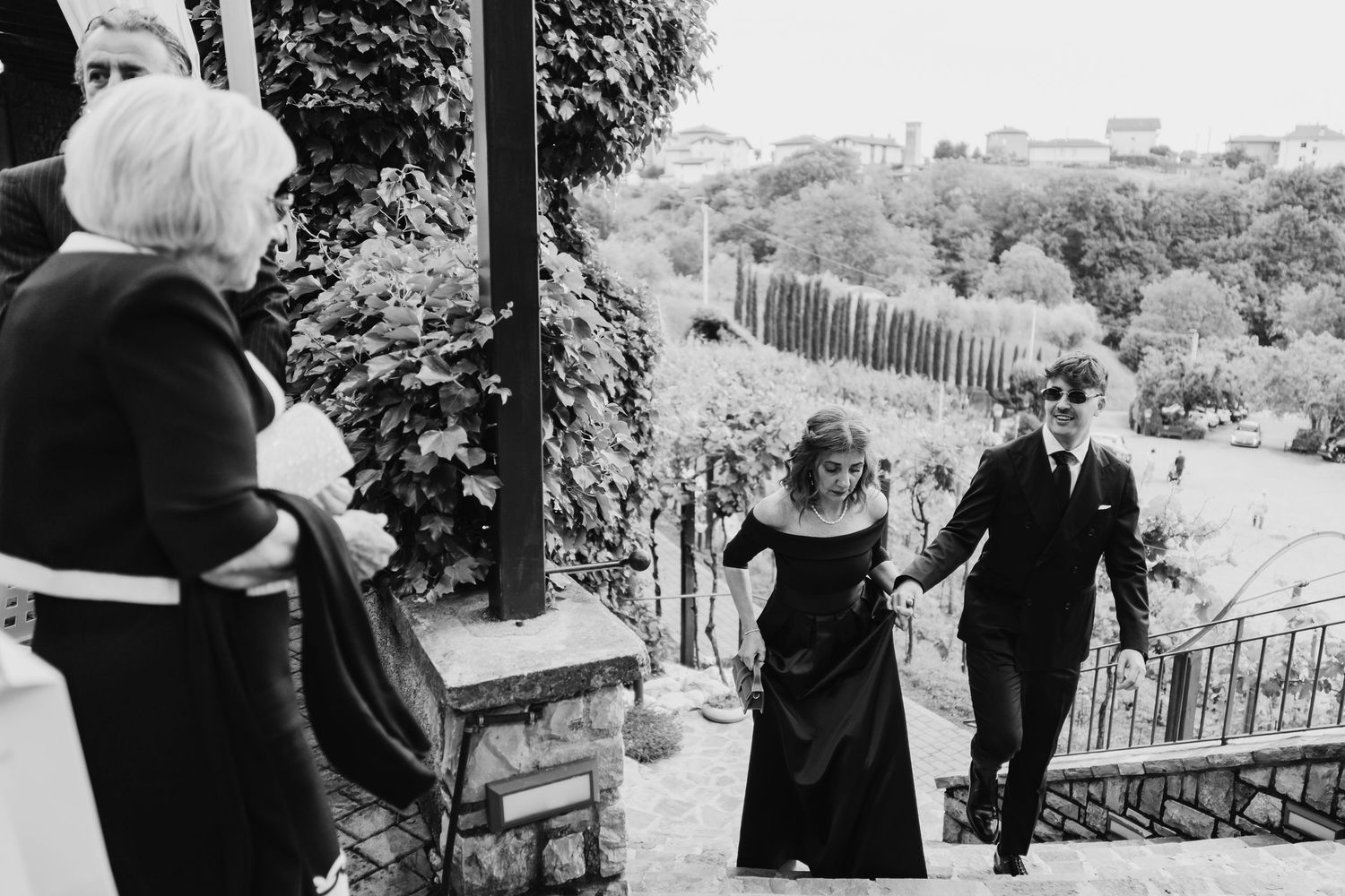 Black and white photo of a couple in formal attire climbing stone steps at a vineyard wedding.
