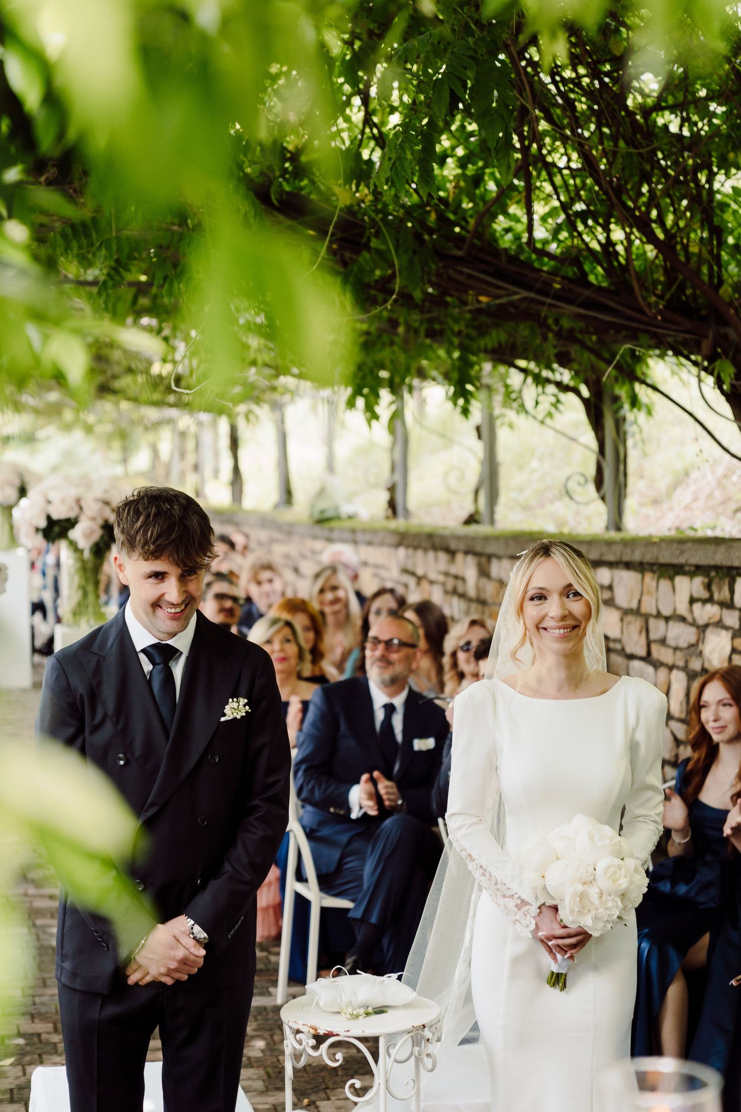 Smiling bride and groom stand at the altar during an outdoor garden wedding ceremony.