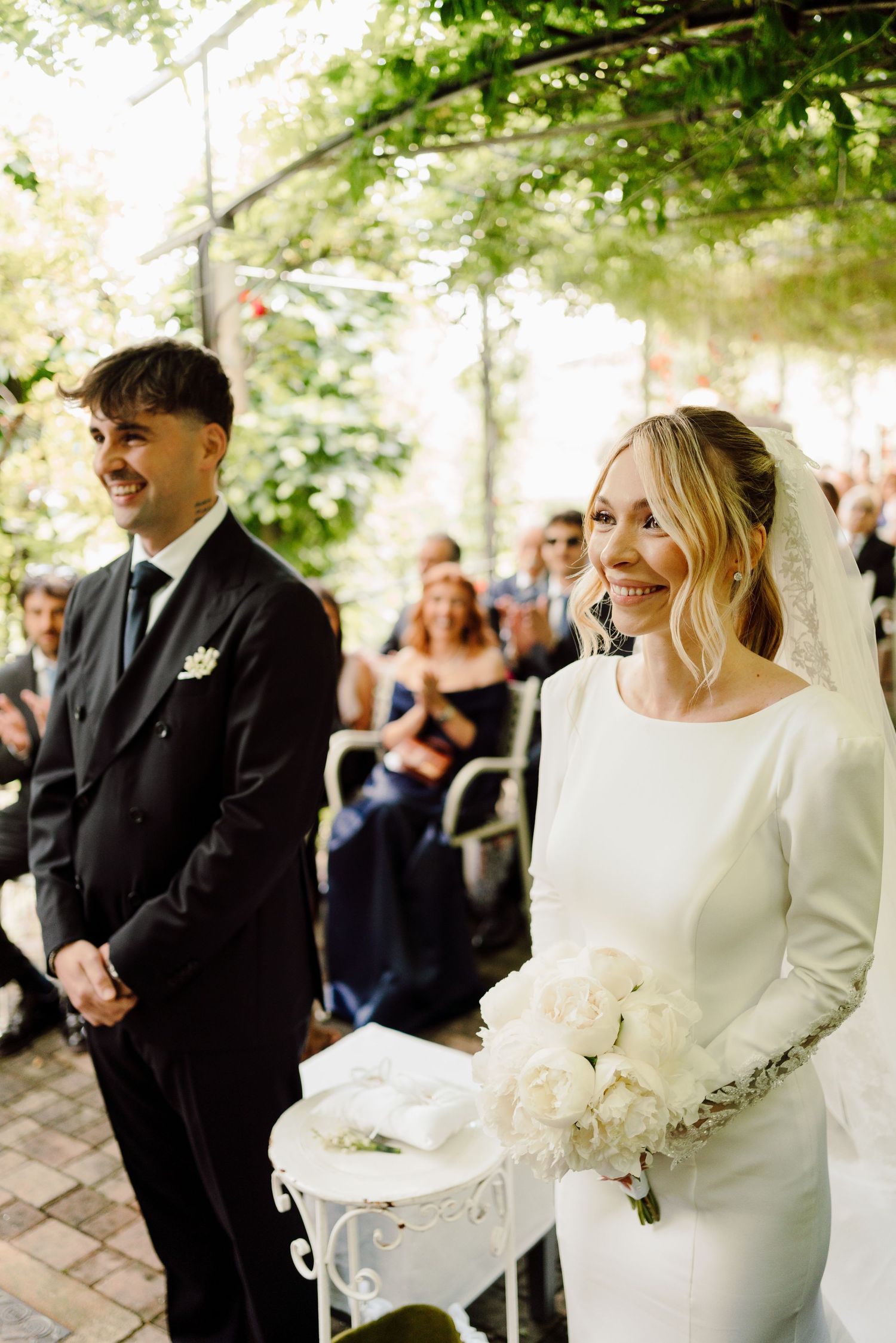 Joyful bride and groom smile at the altar during a sunlit outdoor wedding ceremony.