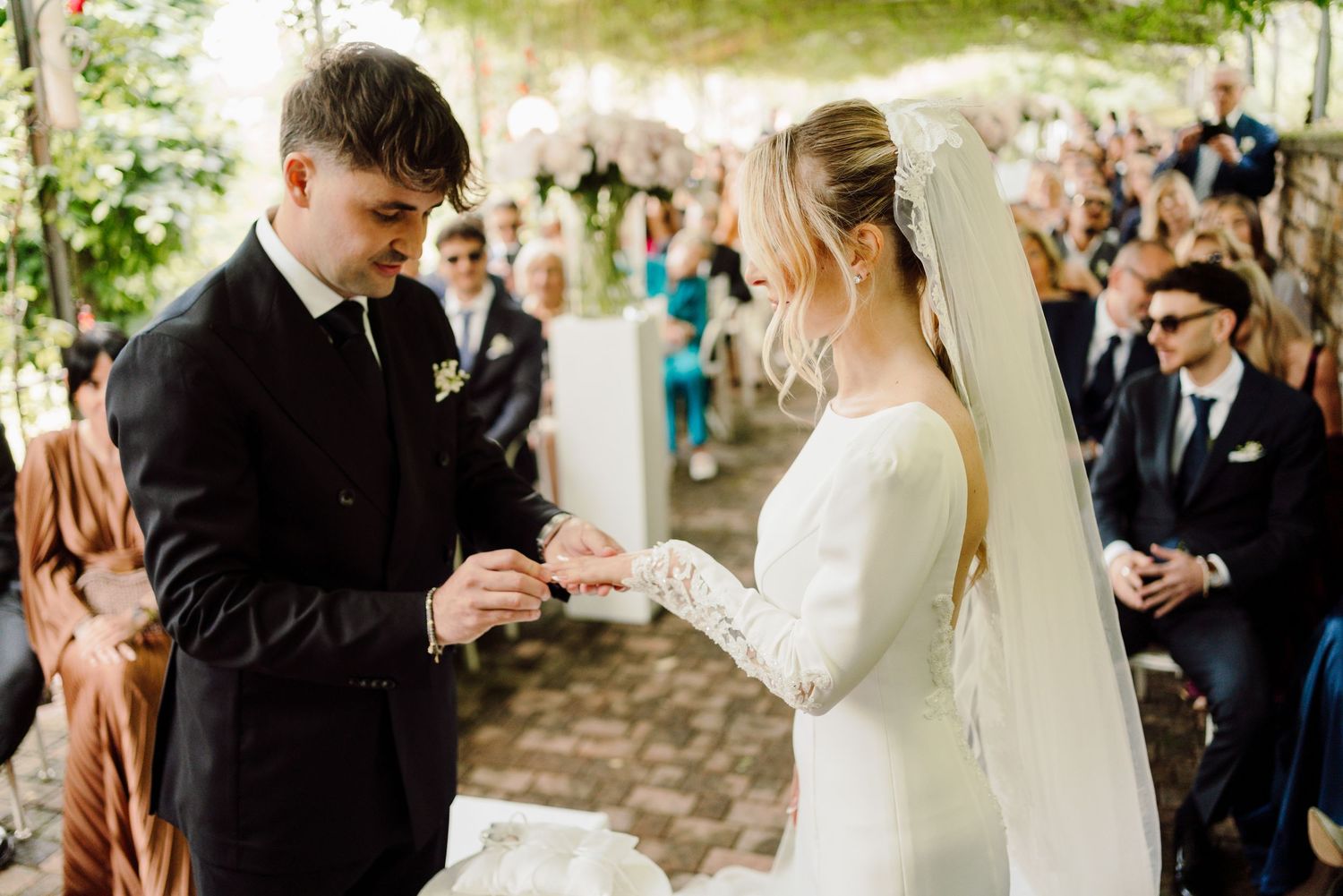 Groom places wedding ring on brides finger during an intimate outdoor ceremony.