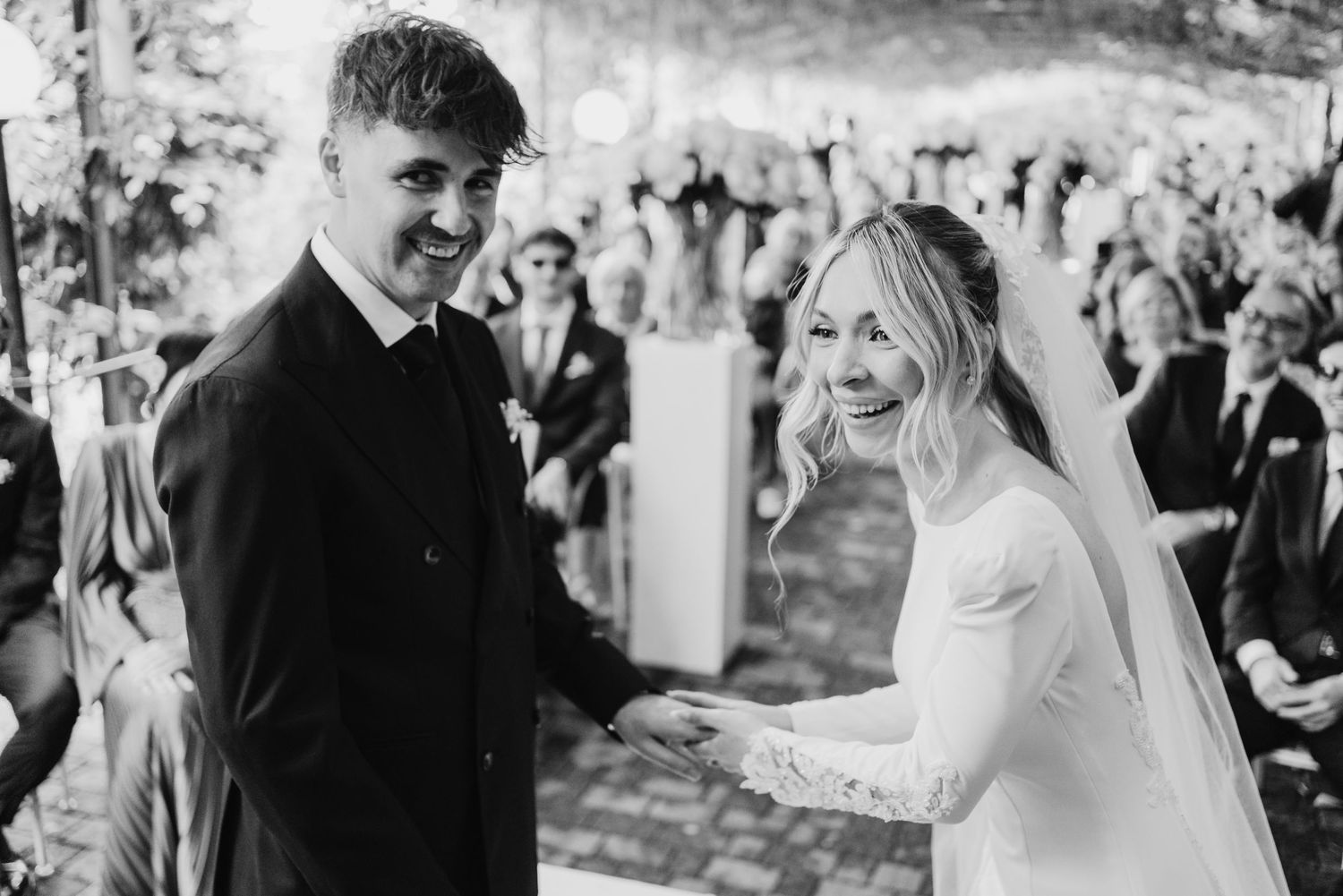 Bride and groom smile joyfully while holding hands after exchanging vows in black and white.