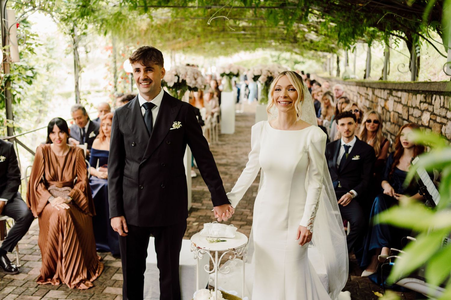 Smiling bride and groom holding hands while walking down the aisle at outdoor wedding.