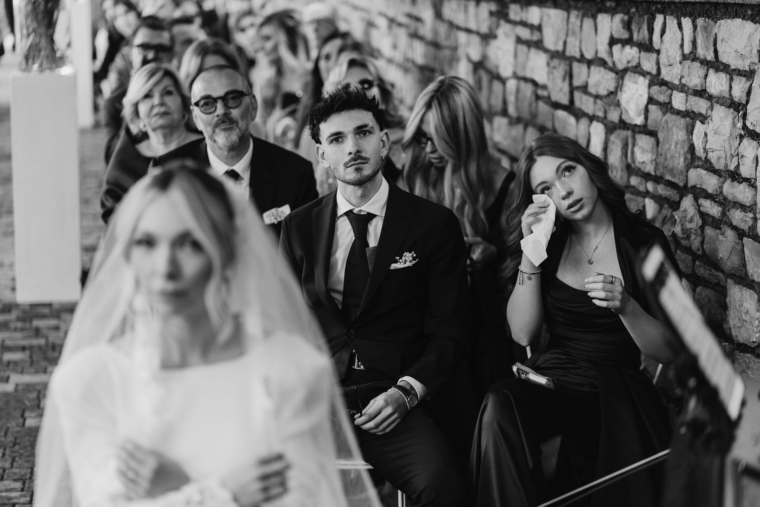 Emotional wedding guests wiping tears during ceremony in black and white photography.