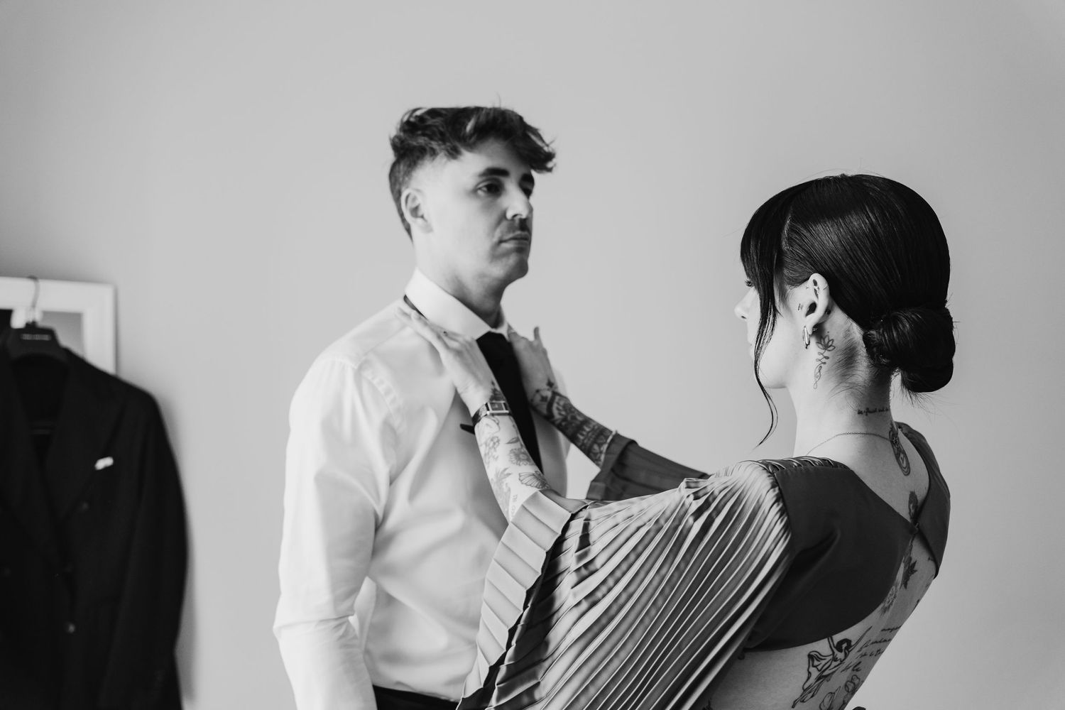 Black and white photo of woman helping groom adjust tie before wedding ceremony.