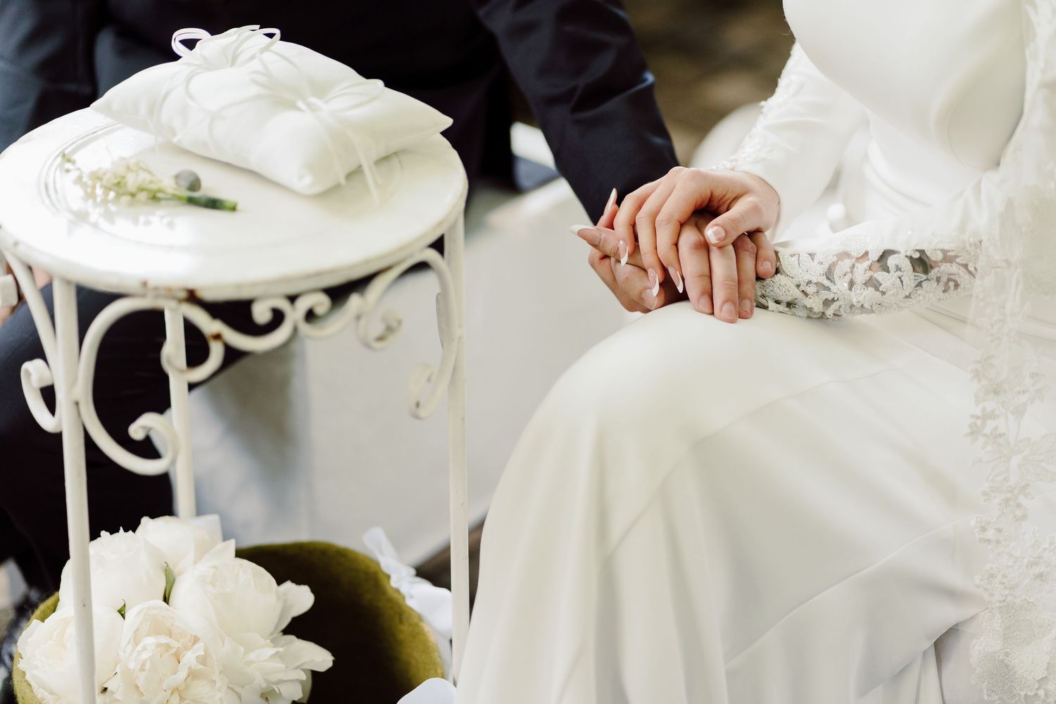 Bride and groom holding hands near decorative white table with wedding rings during ceremony.
