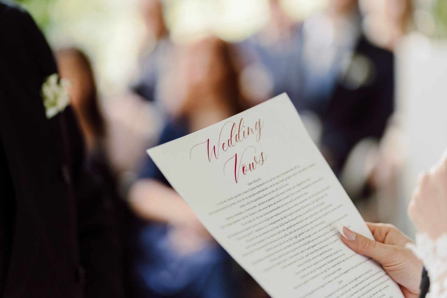 Close-up of hands holding a Wedding Vows card during an outdoor wedding ceremony.