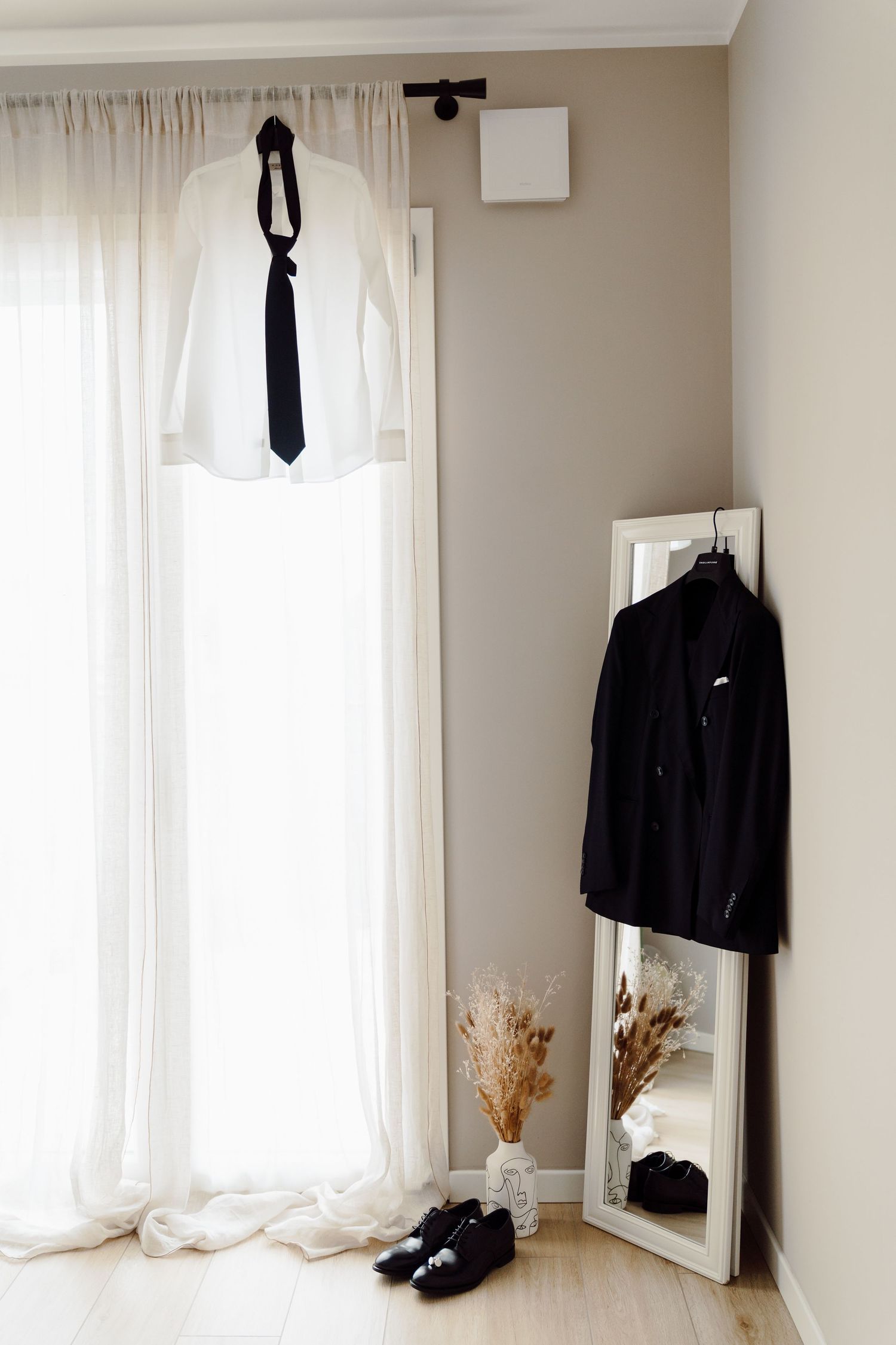 Groom wedding outfit flat lay with white shirt, black tie, suit jacket, and dress shoes by mirror.