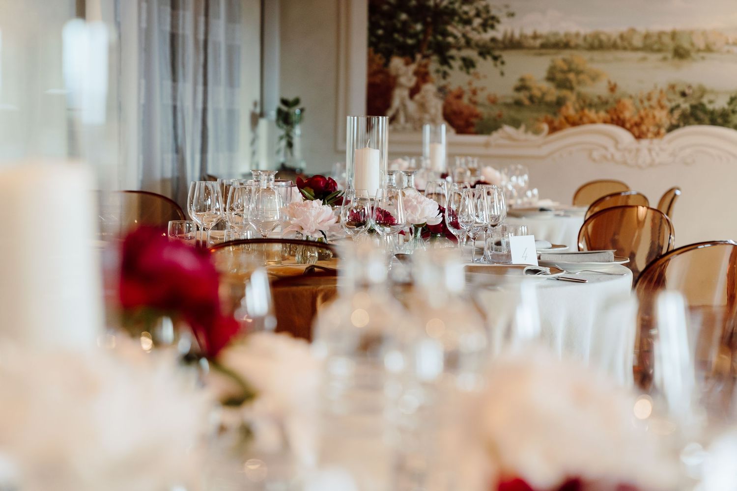 Elegant wedding reception table set with crystal glasses, white candles, and red floral centerpieces.