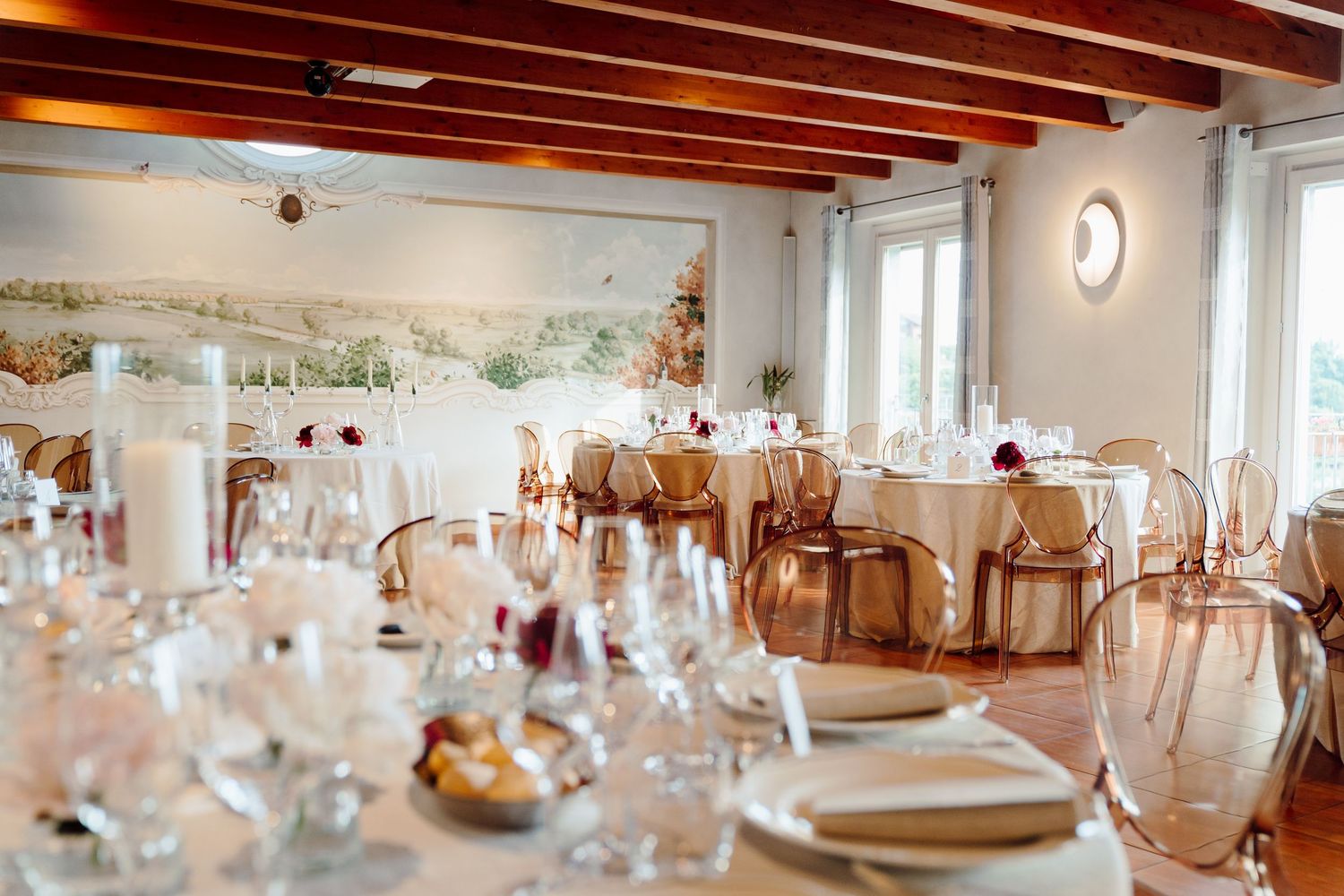 Bright wedding reception venue with wooden beam ceiling, round tables, and elegant place settings.