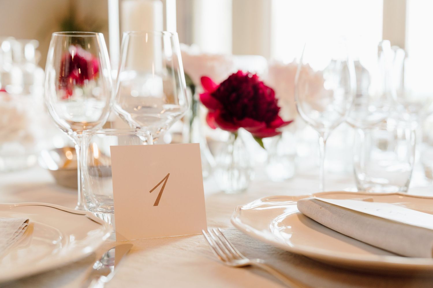 Wedding table number one card displayed beside crystal glasses and red peony centerpiece.