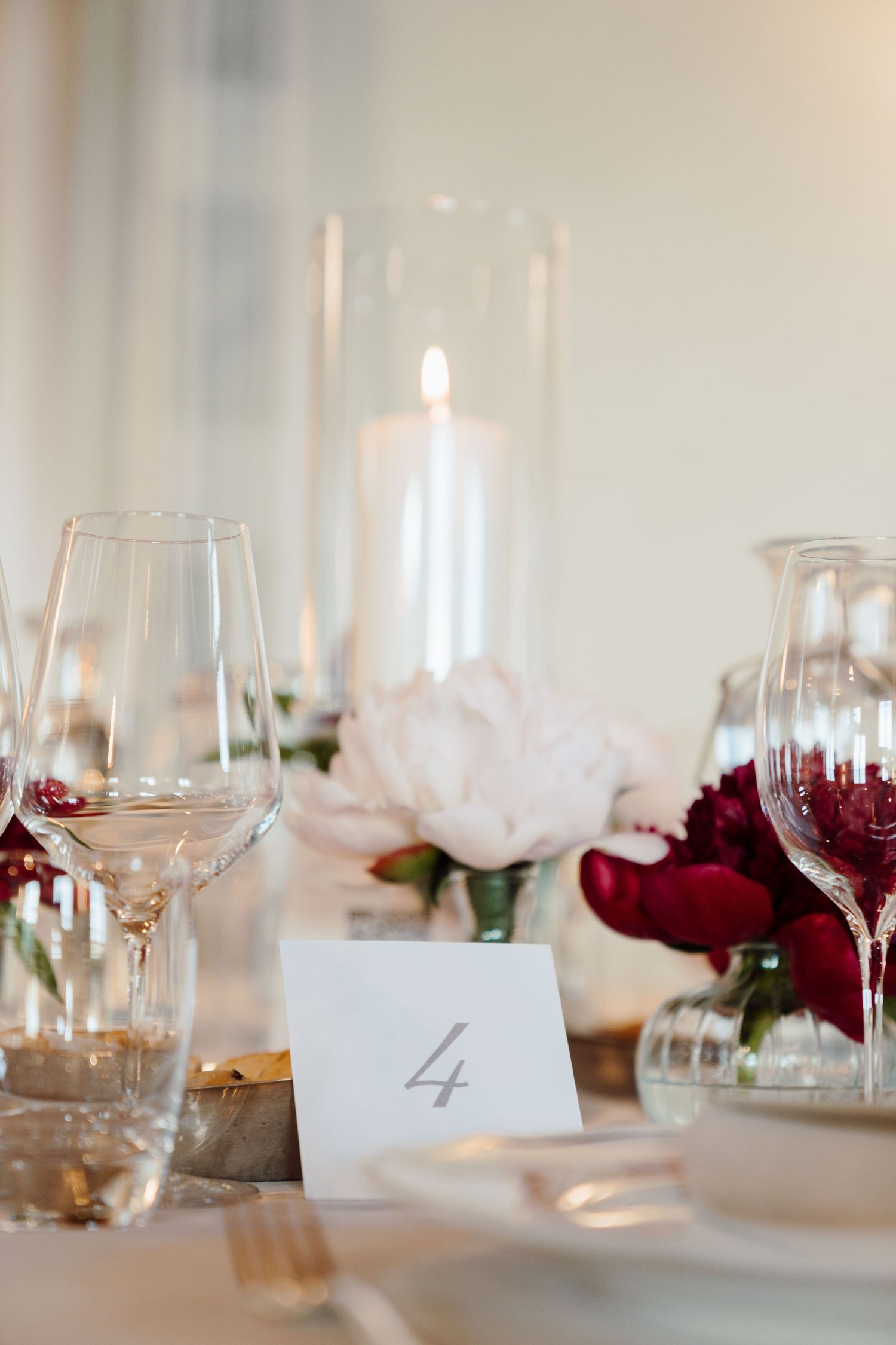 Wedding table number four card beside lit candle and red and white peony floral arrangement.