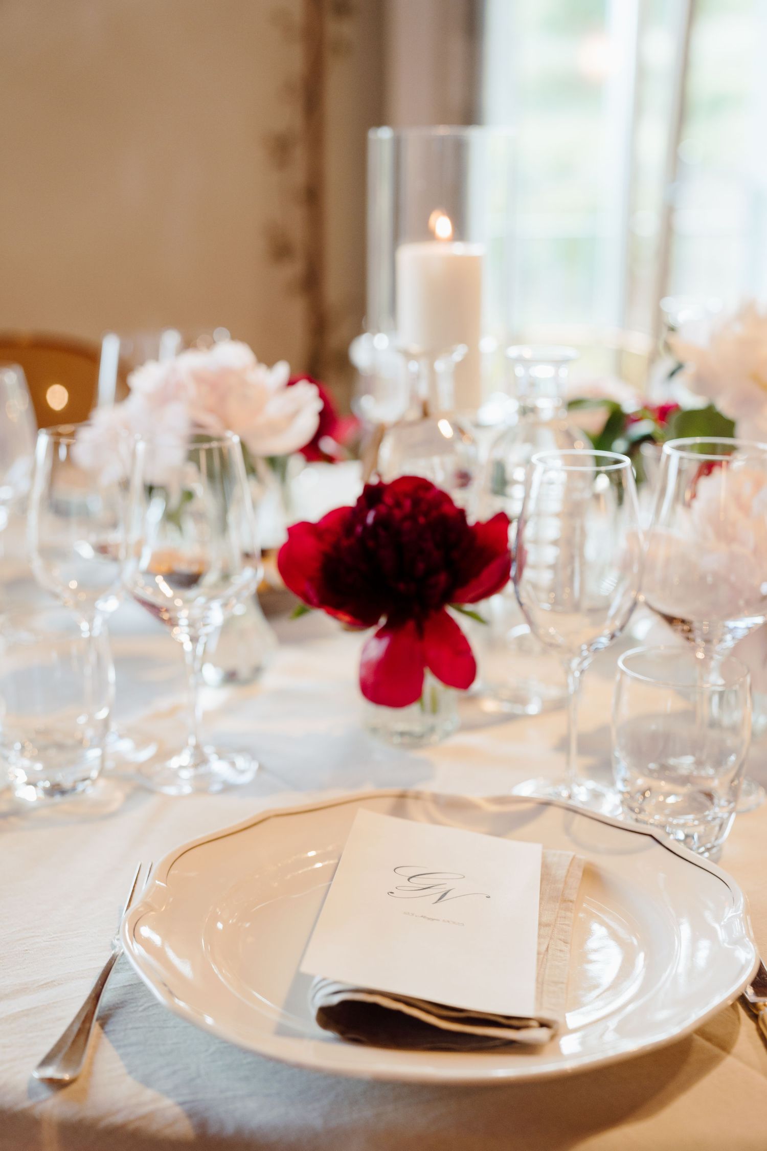 Elegant wedding place setting with monogrammed menu card, crystal glasses, and red peony centerpiece.