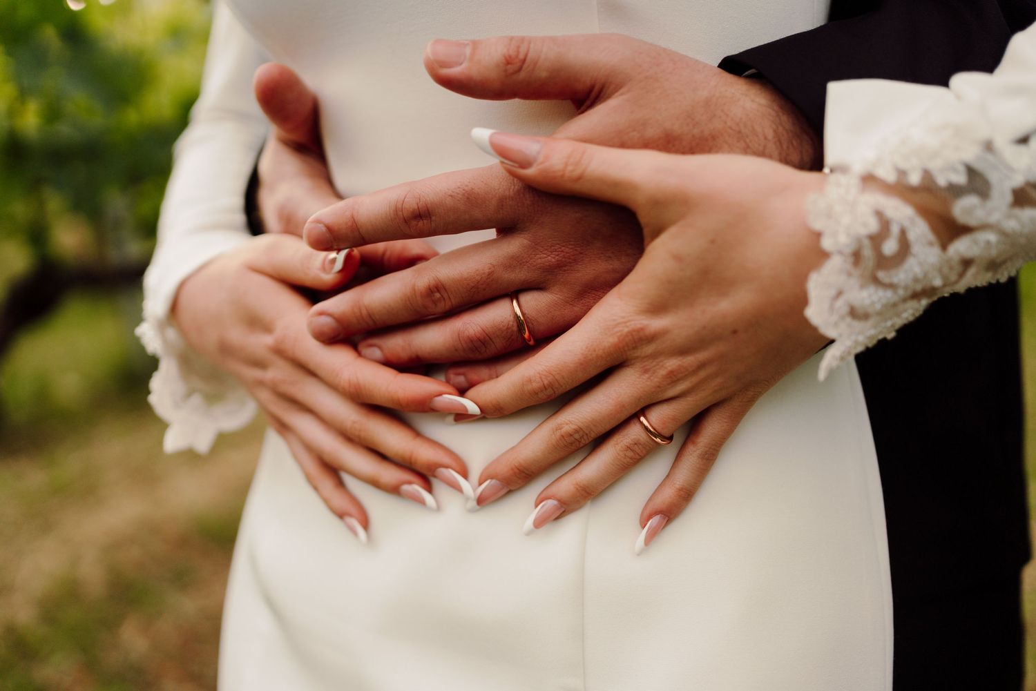 Close-up of bride and groom's hands with wedding rings resting on bride's white gown.