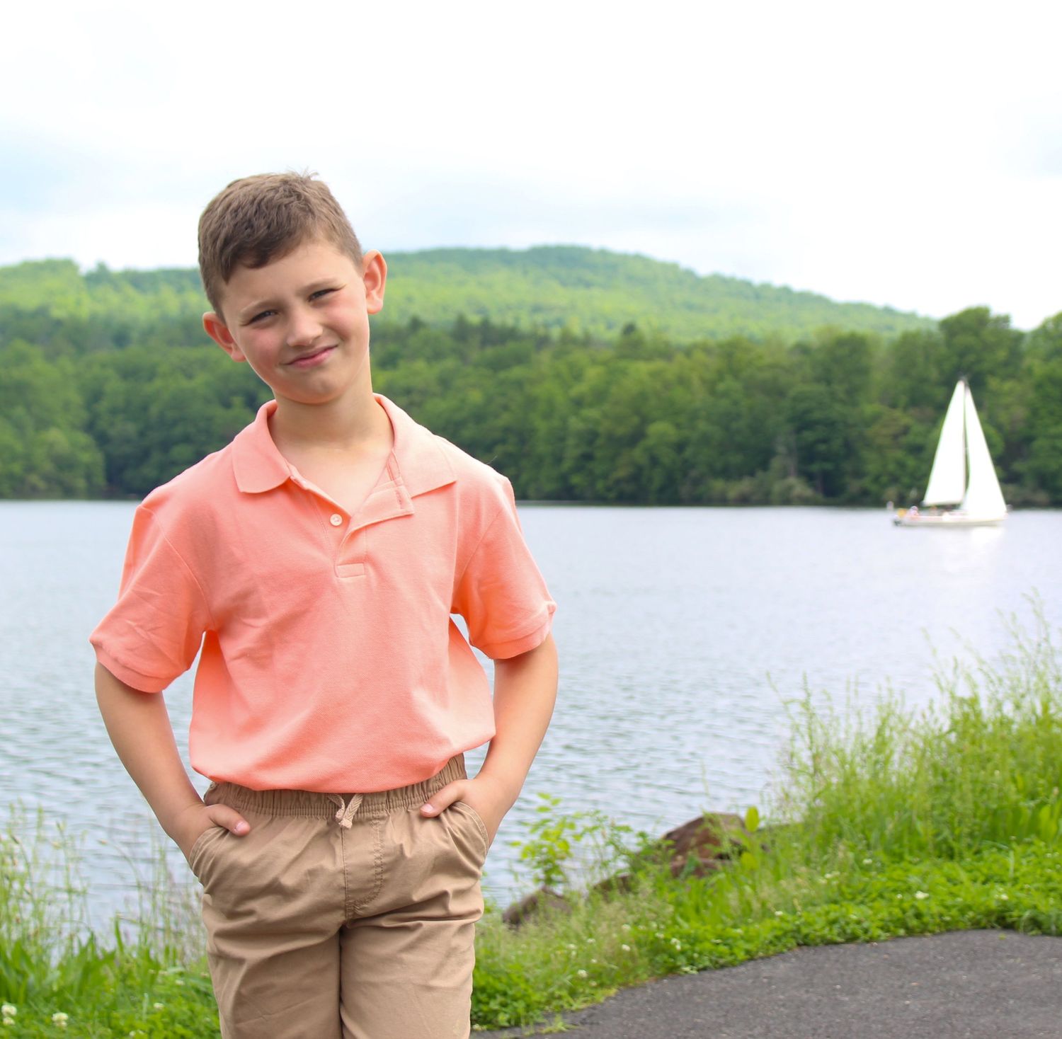 Young person standing by lakeside path with sailboat visible on water, sailboat, brother, lake
