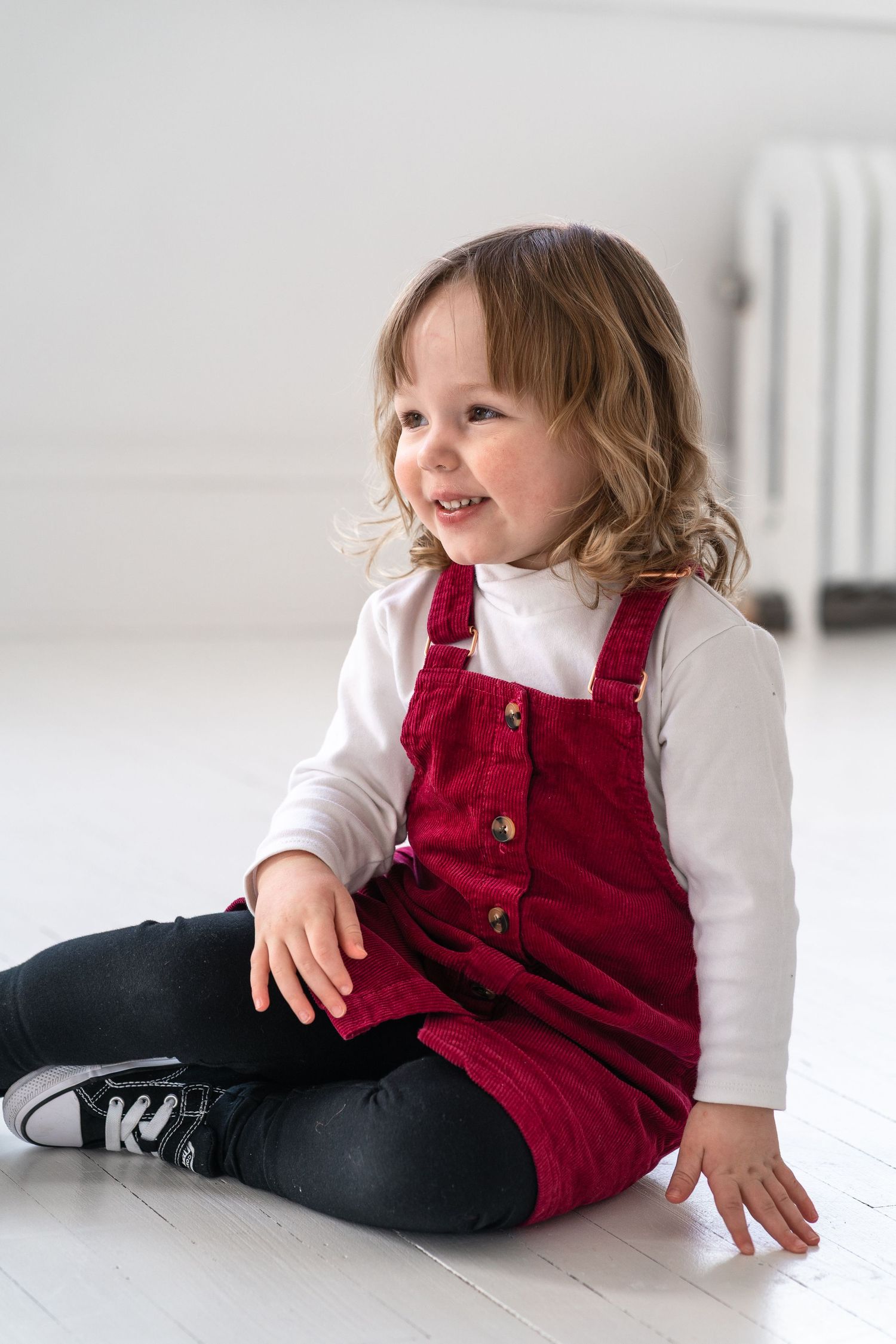 Child in red corduroy overalls and white shirt resting on white floor.