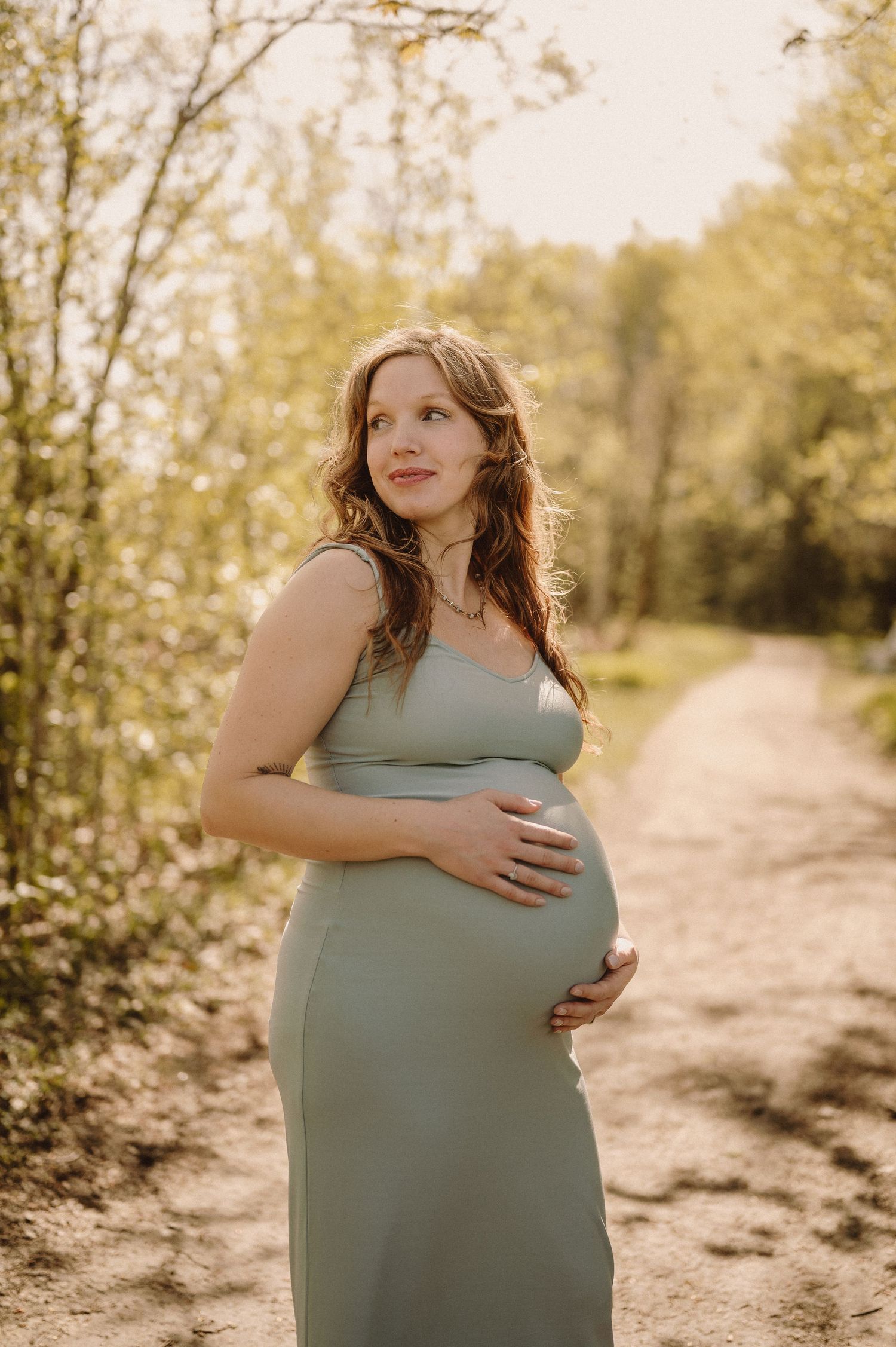 Expecting mother in a blue dress poses on a sunlit nature path.