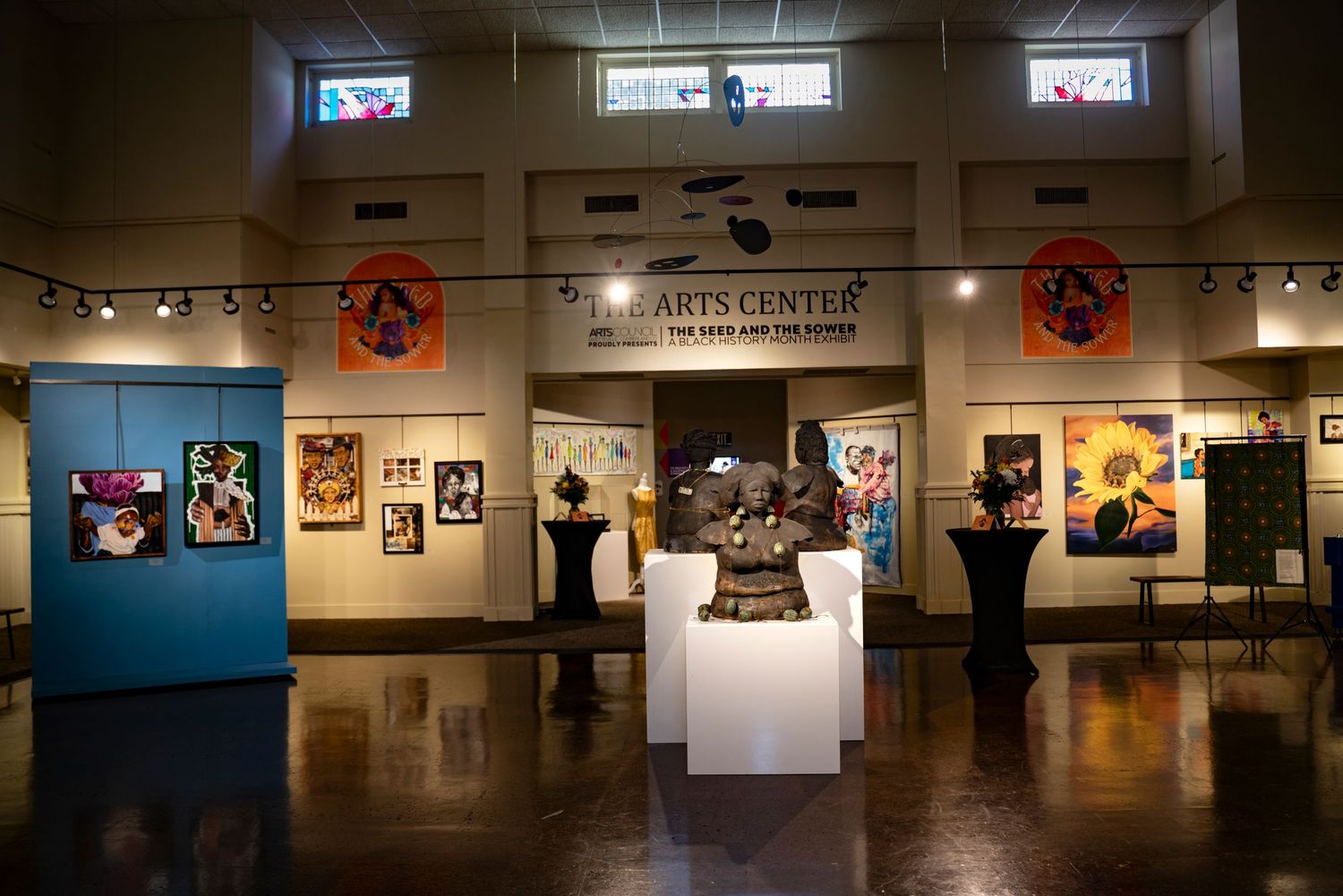 Interior of arts center gallery showing framed artwork displays and sculptures on pedestals.