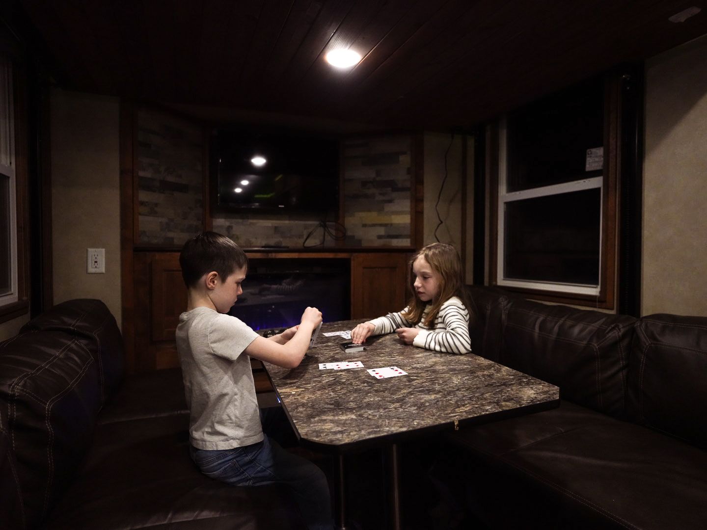 People playing cards at a table inside a cozy RV with wood-paneled walls.