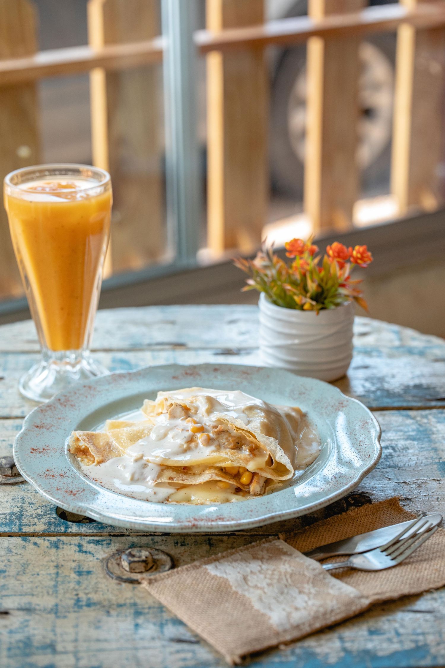 Crepes with whipped cream served alongside orange juice on rustic blue table.