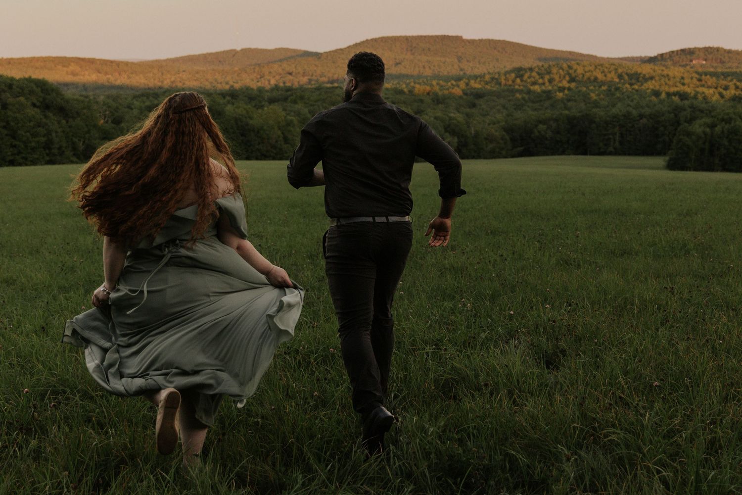 People walking through a scenic meadow at sunset with mountains in the background.