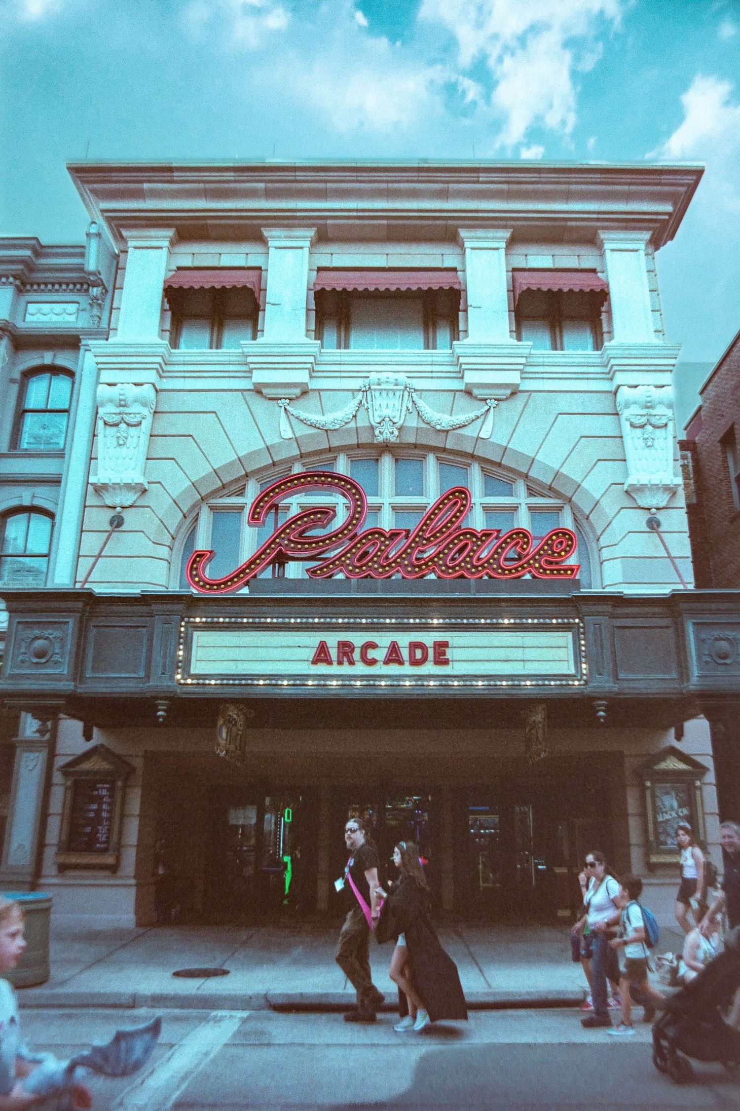 Vintage Palace Arcade building entrance with neon signage and classic architecture against a turquoise sky.