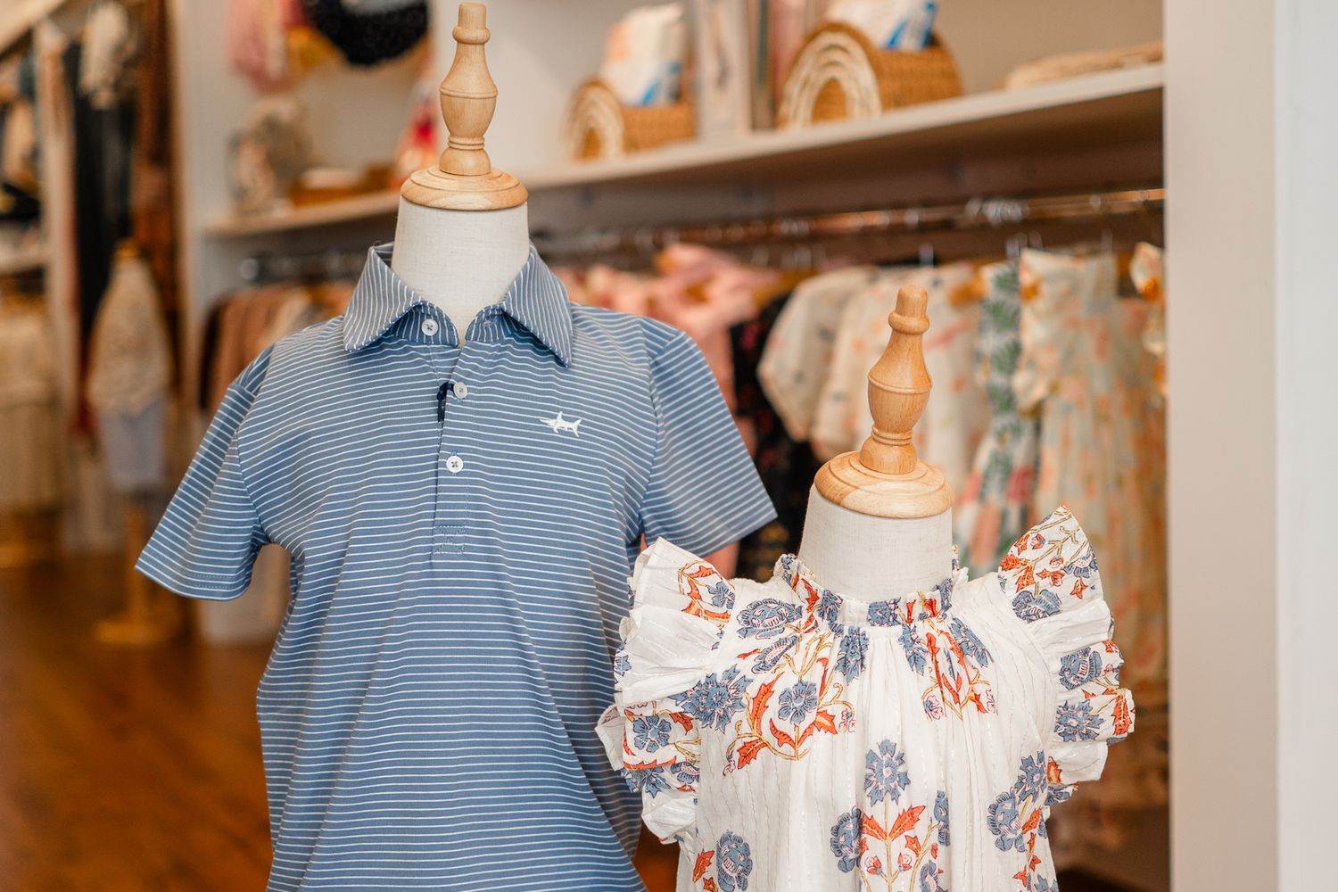 Children's boutique clothing display featuring a blue striped polo shirt and floral print dress on mannequins.