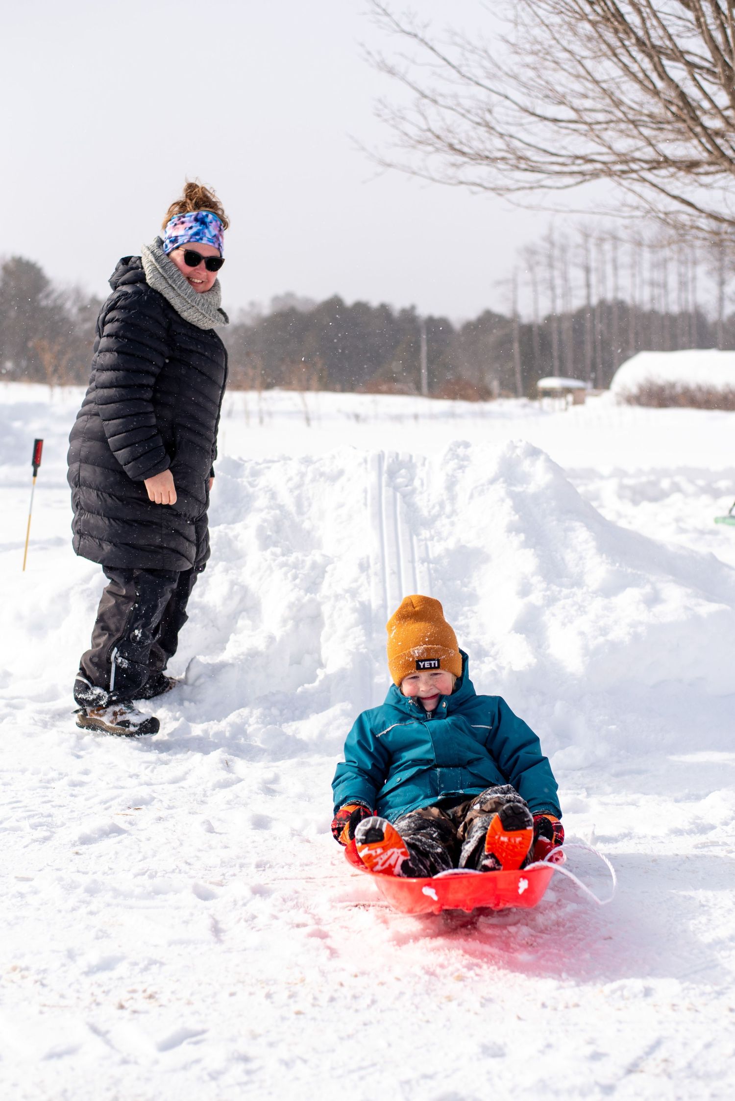 Winter sledding scene with two people enjoying snowy hill activities while wearing warm winter coats and gear.