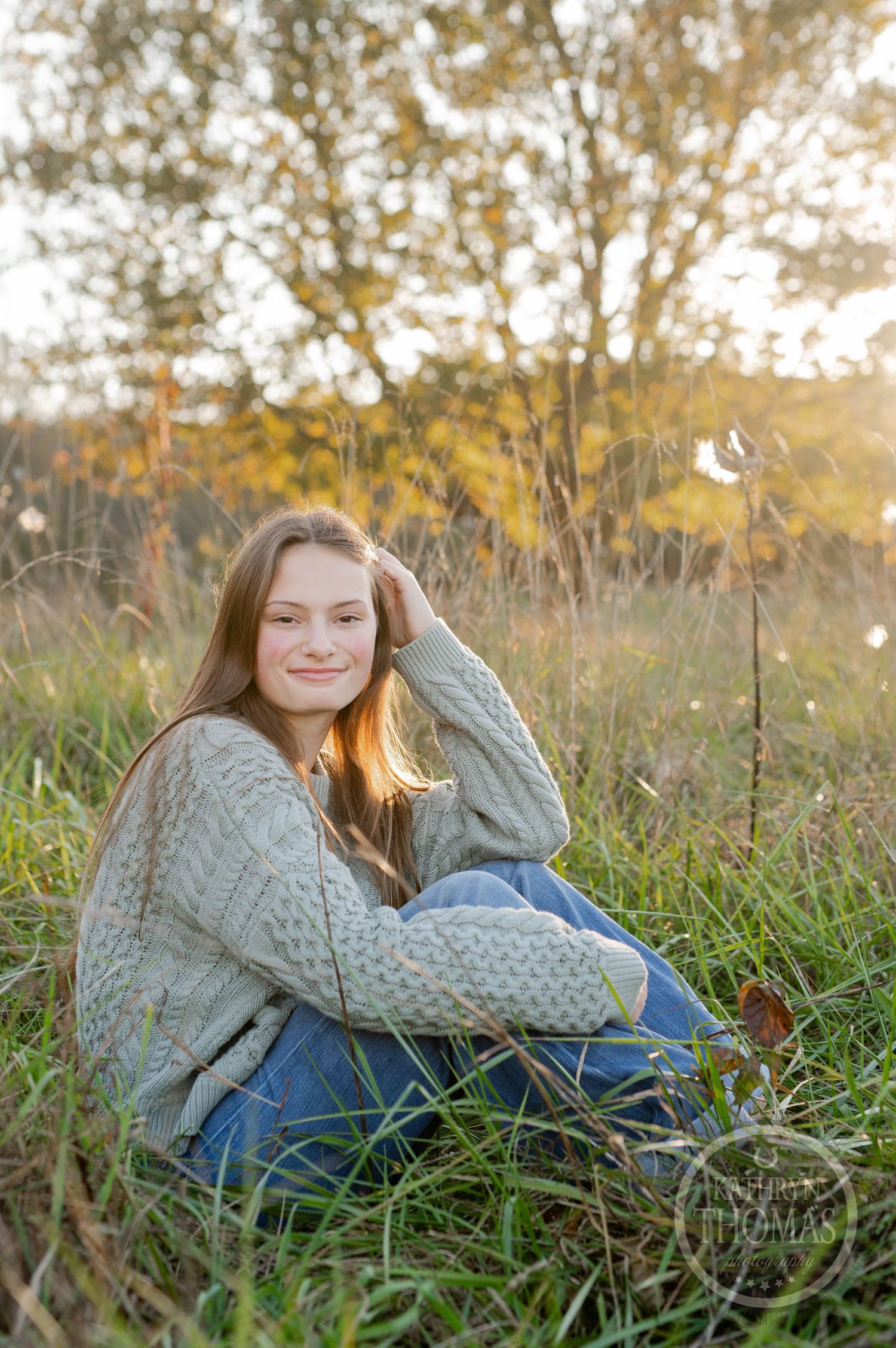 Someone in a cozy knit sweater sits in an autumn field at sunset.