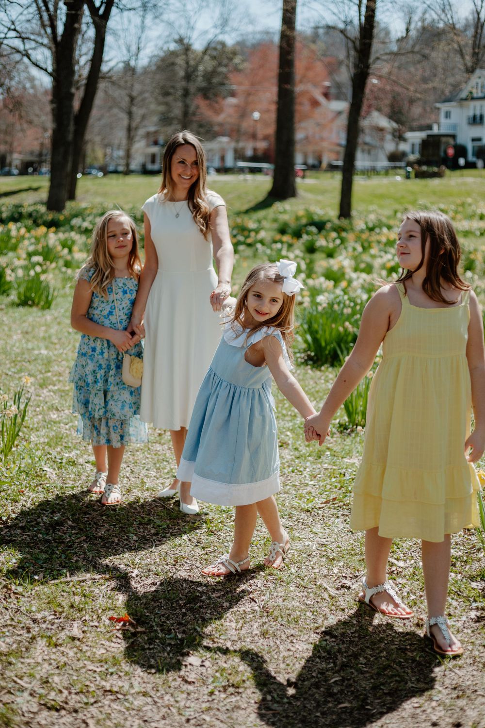 Children in pastel dresses playing and dancing among spring flowers in a park.