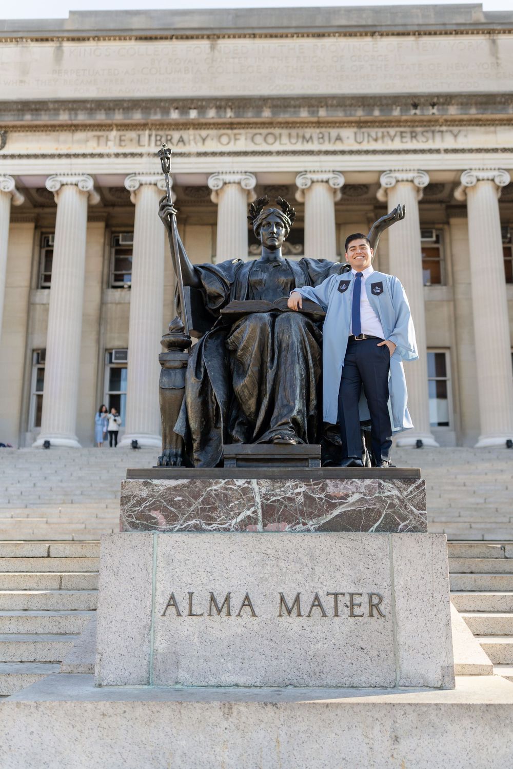 Graduate poses with Alma Mater statue at Columbia University's campus entrance.