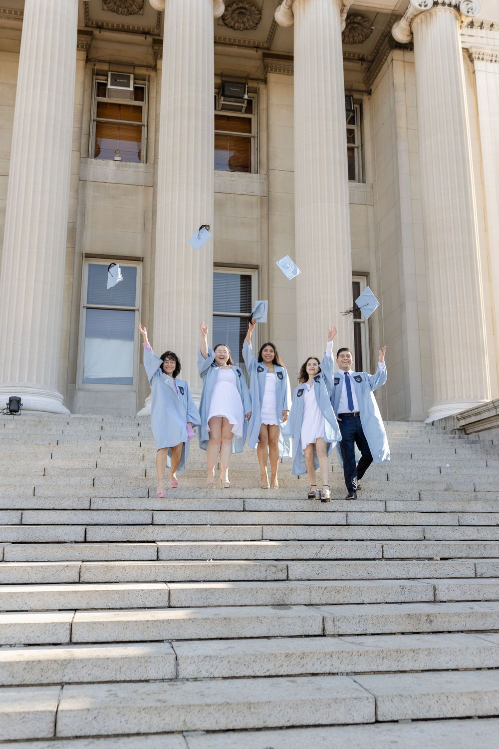 Graduates throw their caps in celebration on the steps of a classical university building.