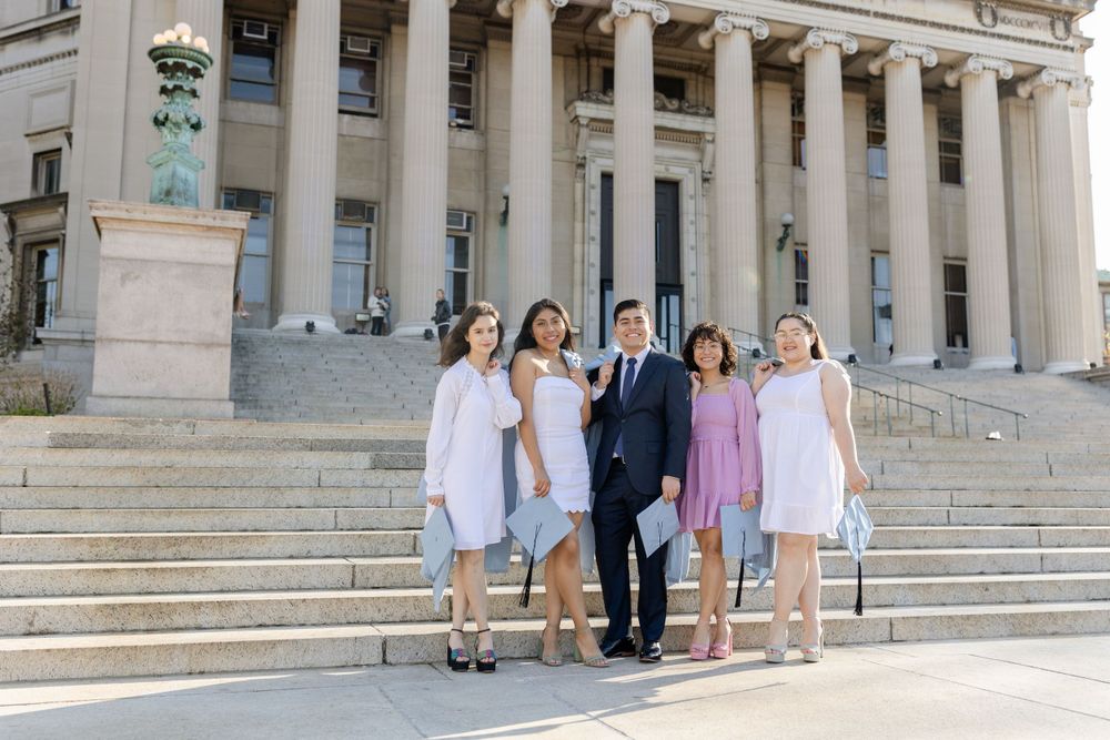 Group stands on the grand steps of a neoclassical university building in formal attire.