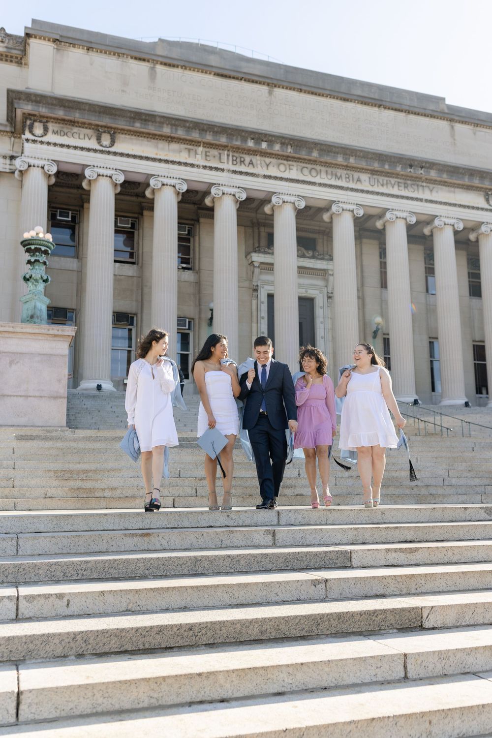 Group descends the stone steps of a classical university building in formal graduation attire.