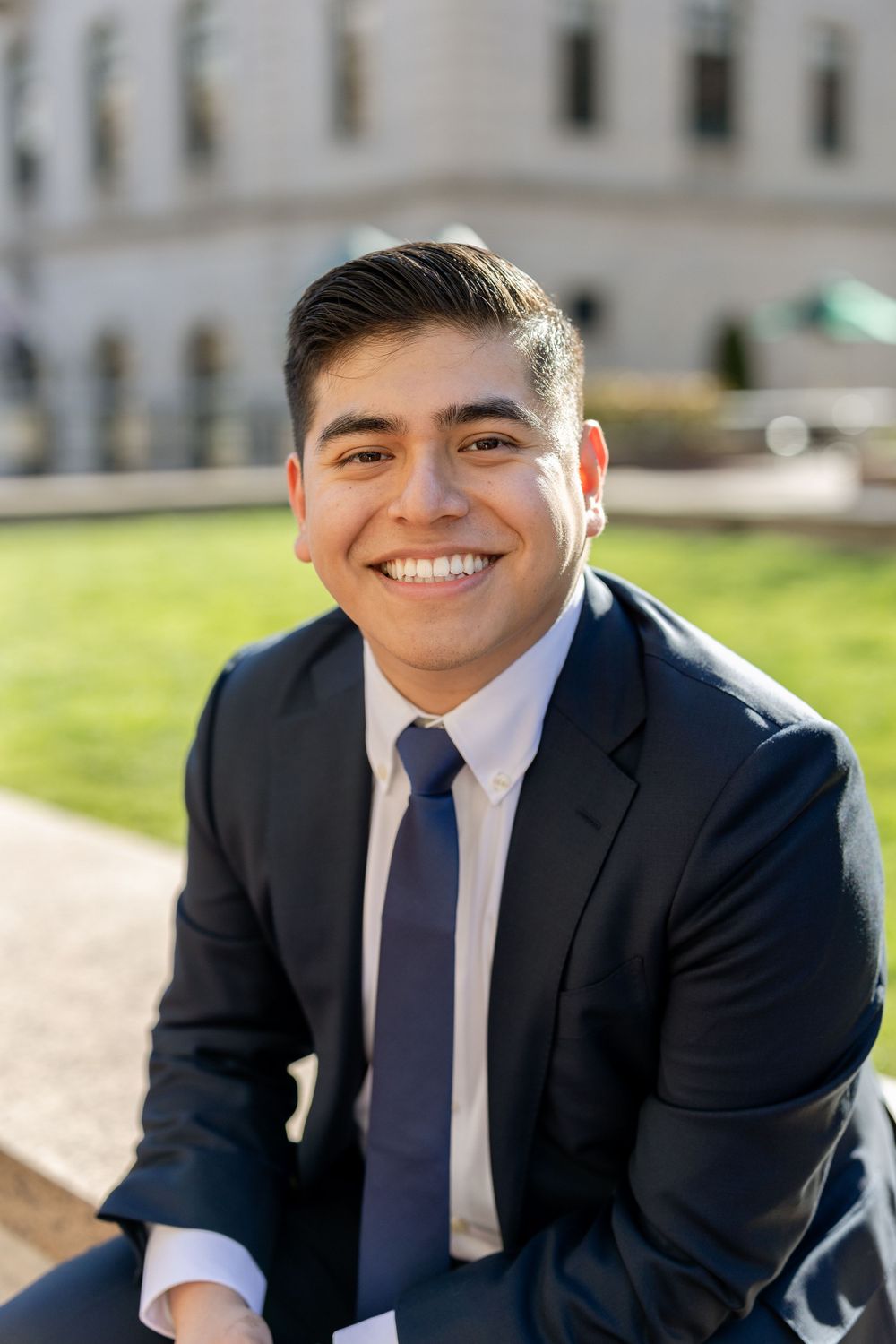 Professional portrait of graduate in navy suit against campus background.