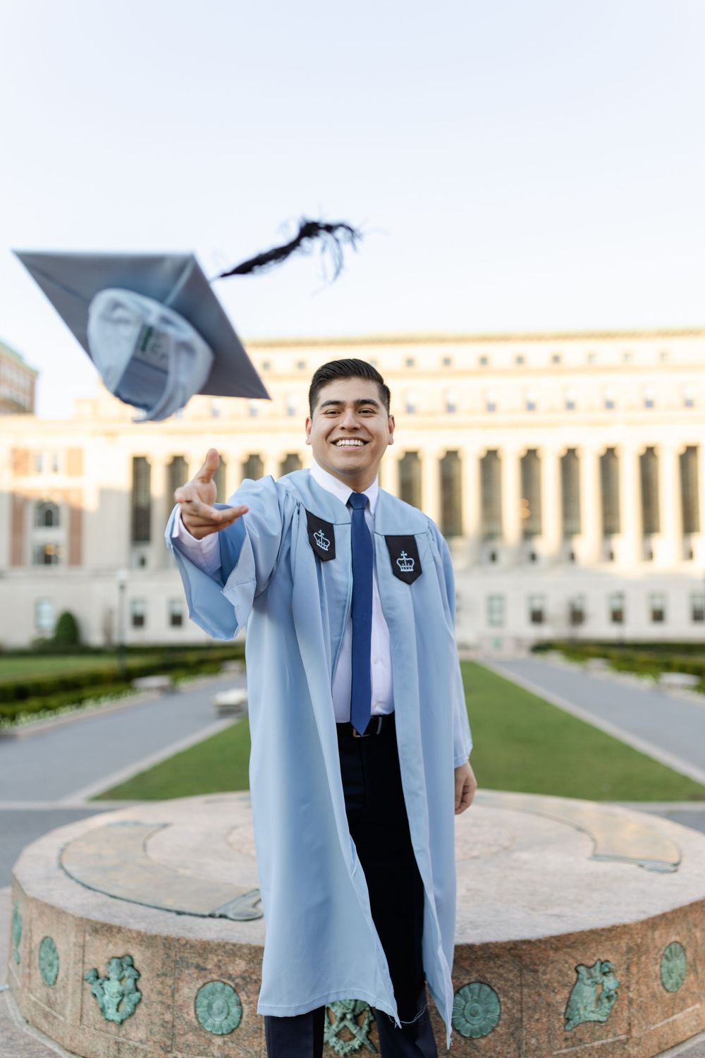 Graduate tosses cap in celebration in front of university building.
