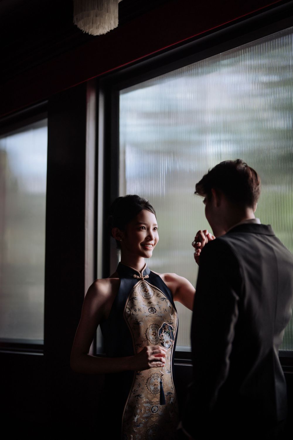 Intimate moment captured in formal wear by window with natural backlighting.
