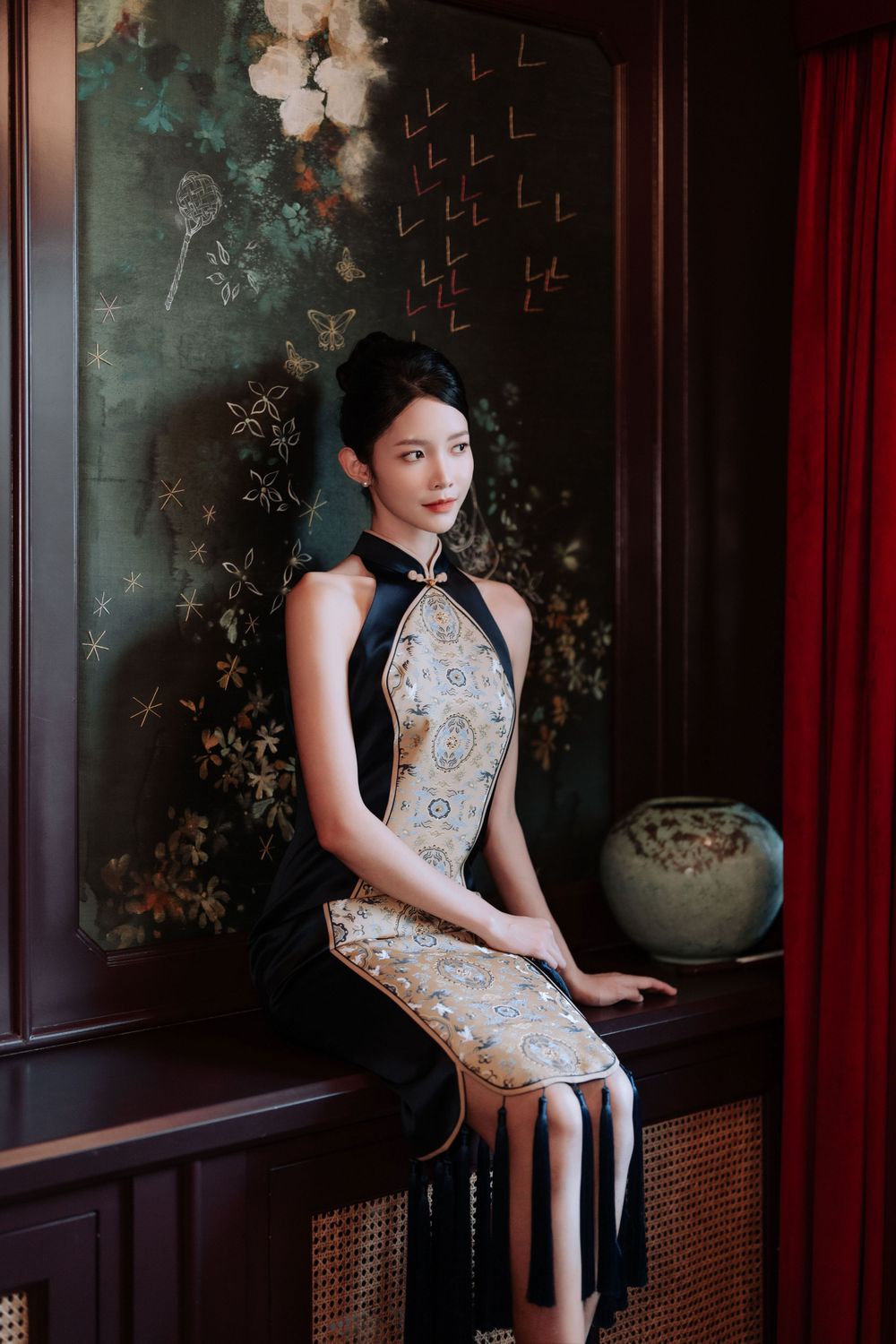 An elegant traditional Chinese qipao dress with floral embroidery details shown in a moody vintage-styled setting.
