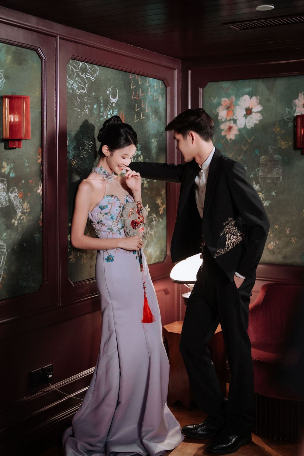Romantic formal couple interaction in vintage-style room with floral wallpaper and mood lighting.