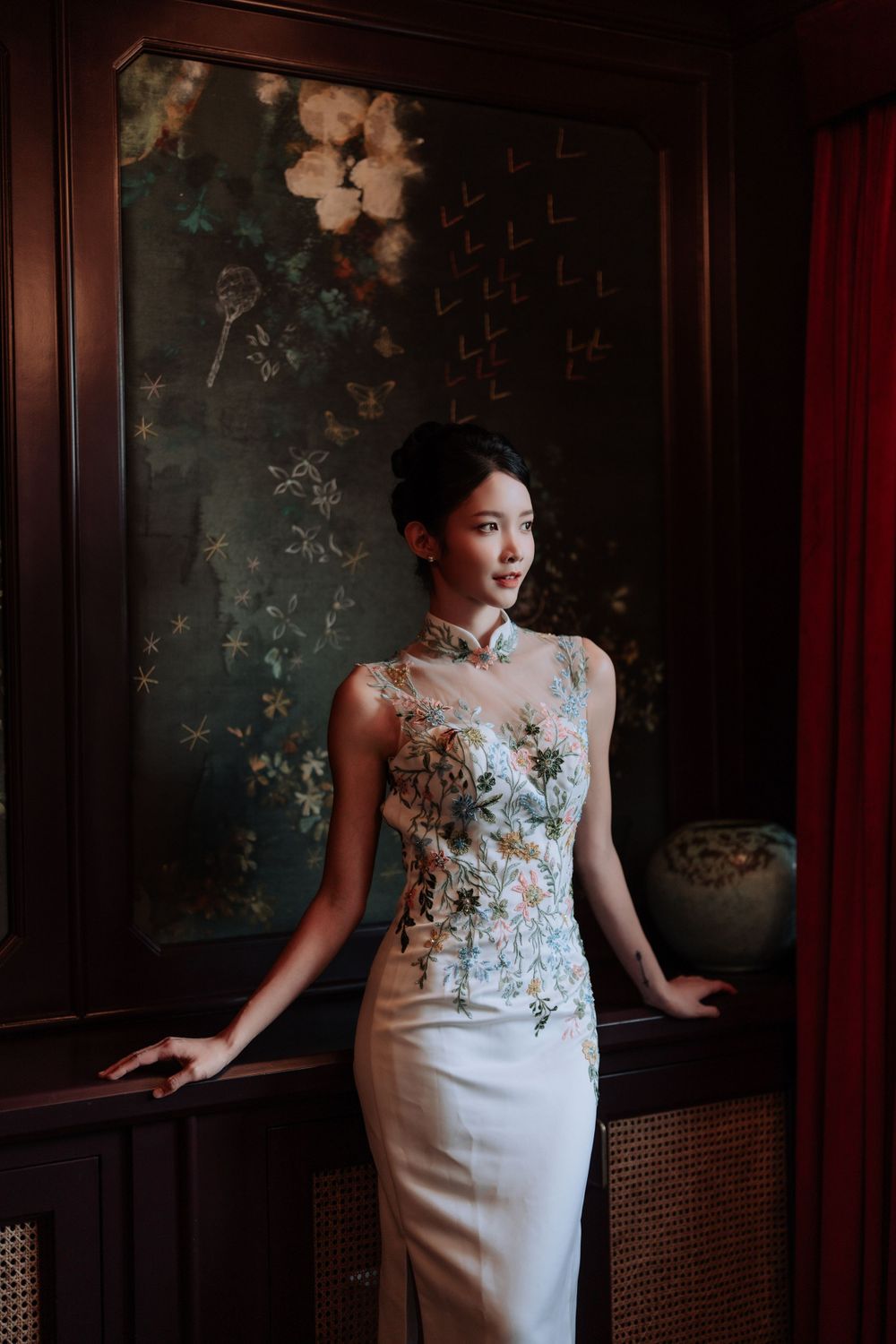 Elegant formal dress featuring a floral embroidered bodice and fitted white skirt in a traditional Asian-inspired setting.